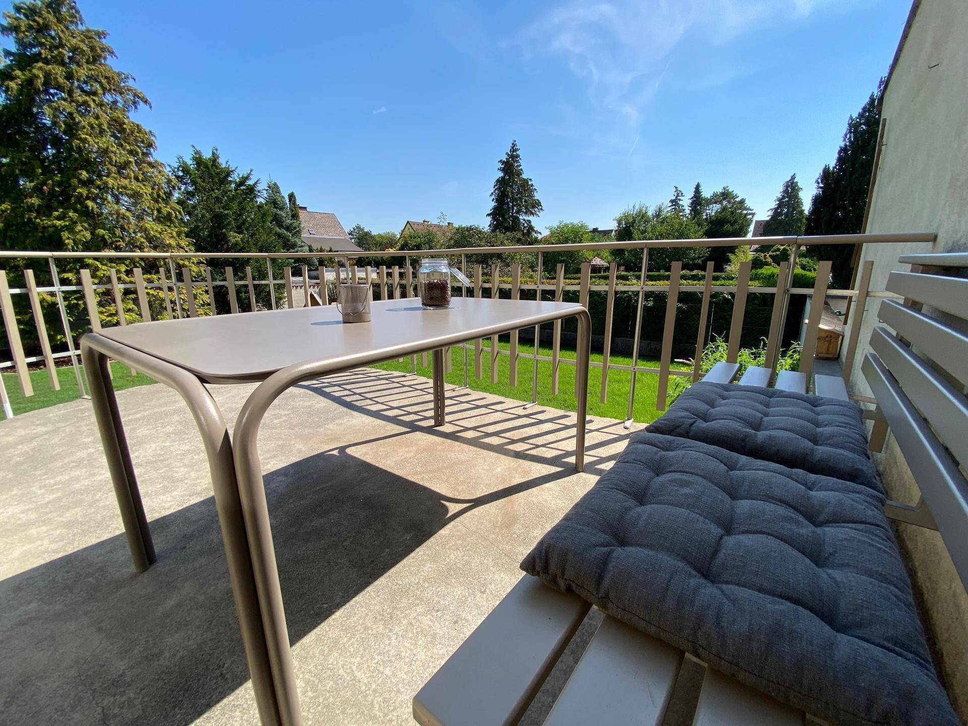 Gemütlicher Balkon mit Gartenmöbeln und einem schönen Ausblick ins Grüne an einem sonnigen Tag.