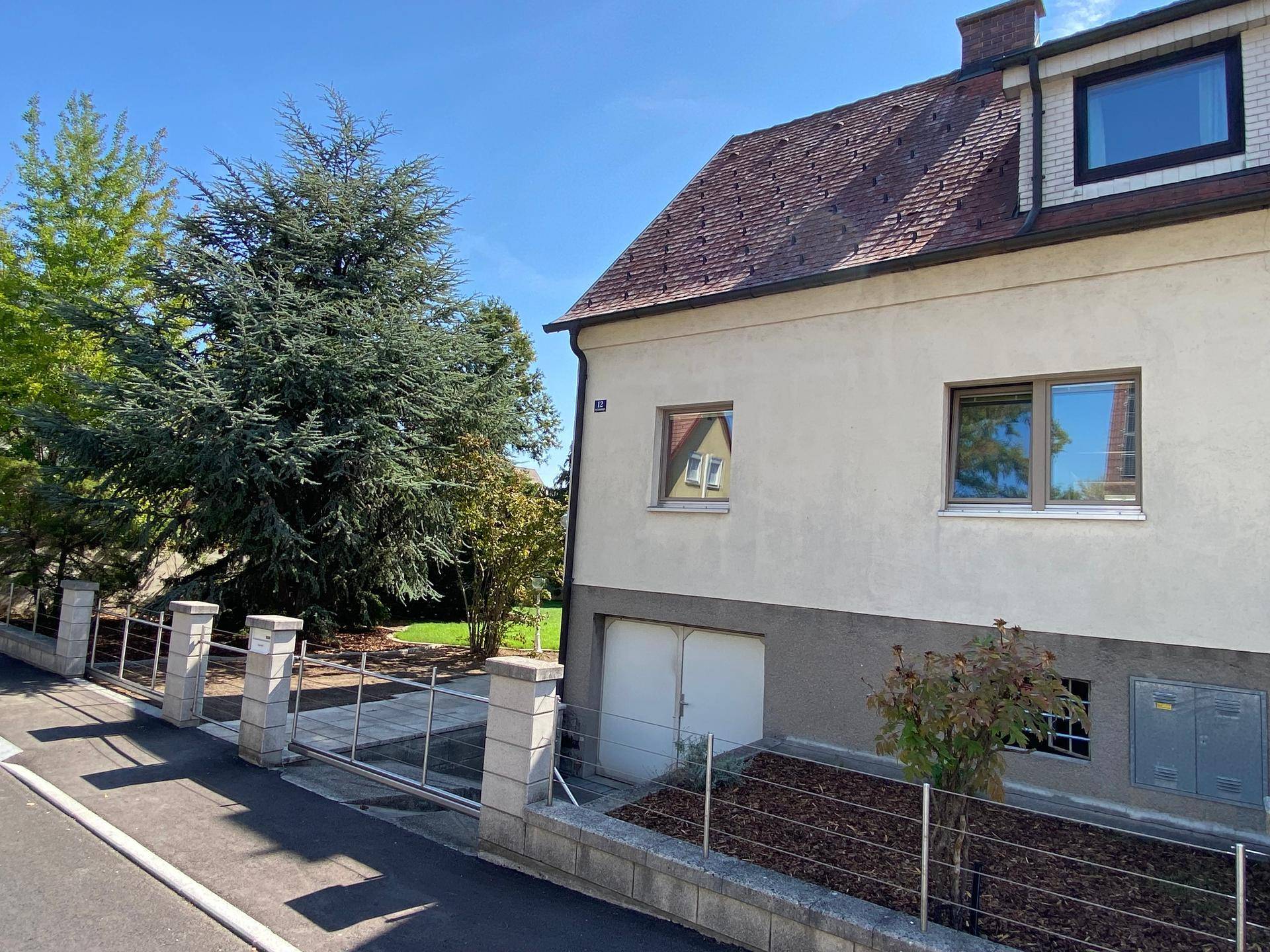 Seitenansicht des Hauses mit Garage, modernen Fenstern und gepflegter Außenanlage.