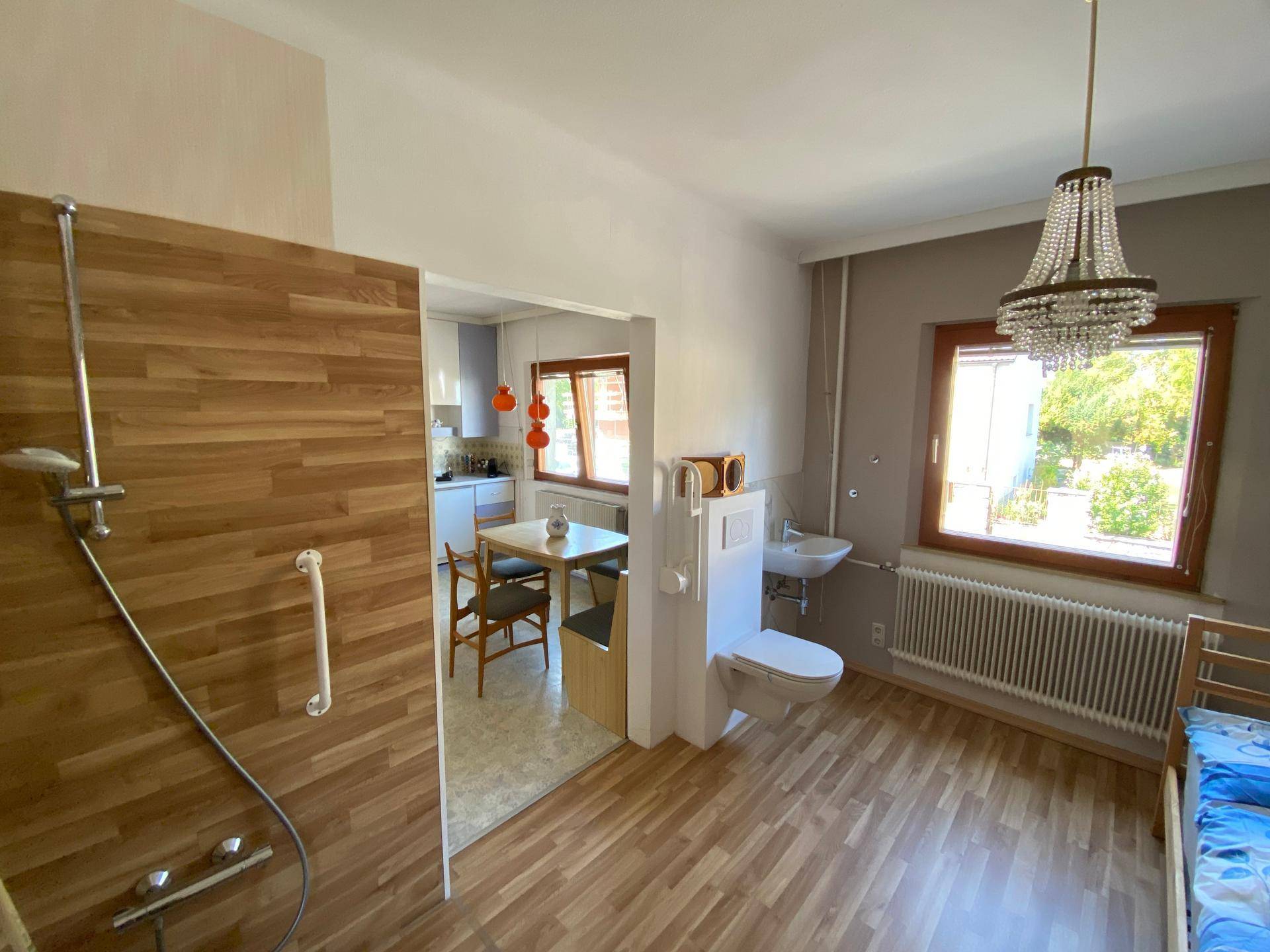 Offener Raum mit Duschbereich, Toilette und Waschbecken, angrenzend an eine Küche.