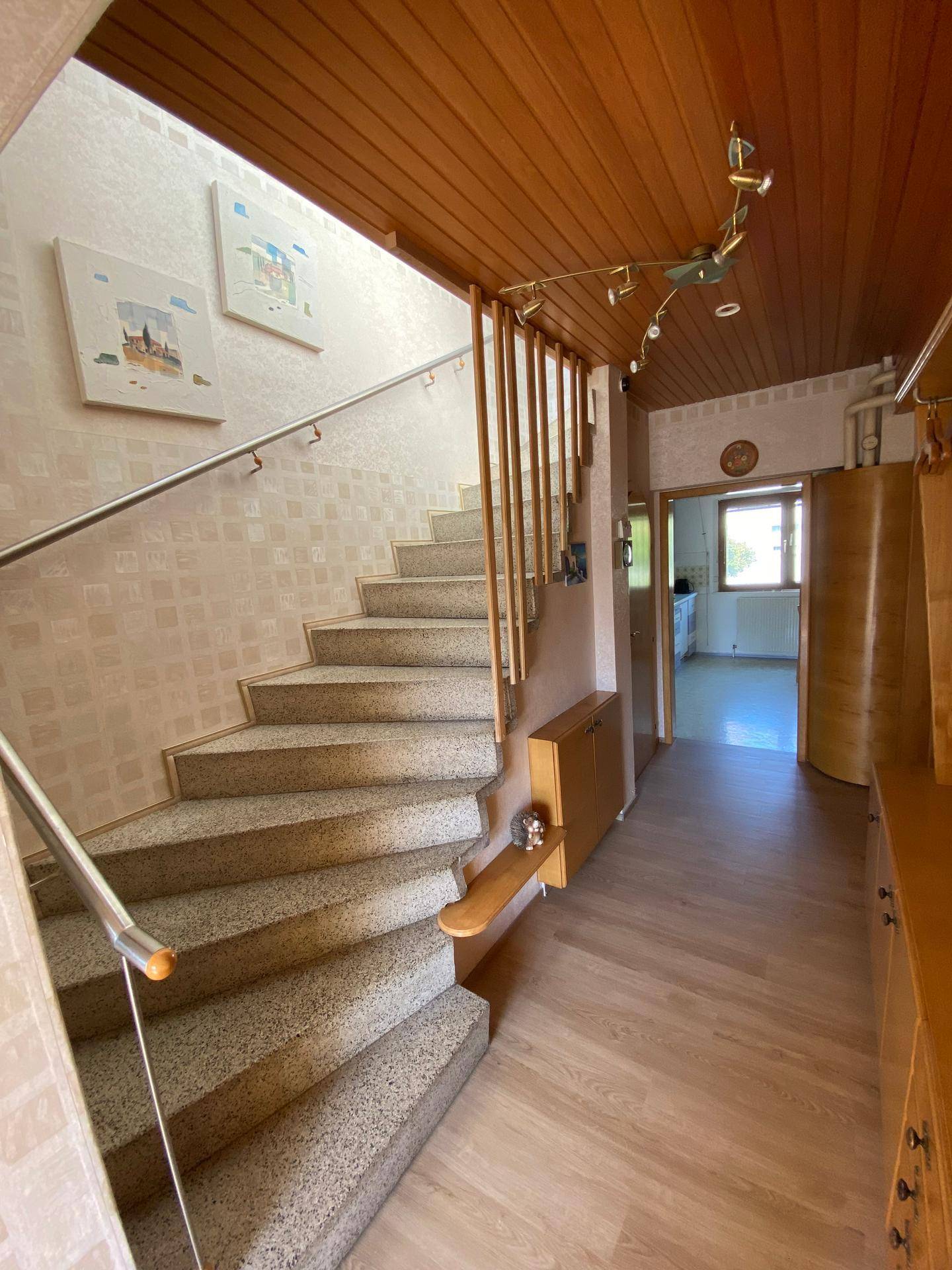 Heller Flur mit Treppe, Holzdecke und gemusterter Tapete, die zu weiteren Räumen führt.