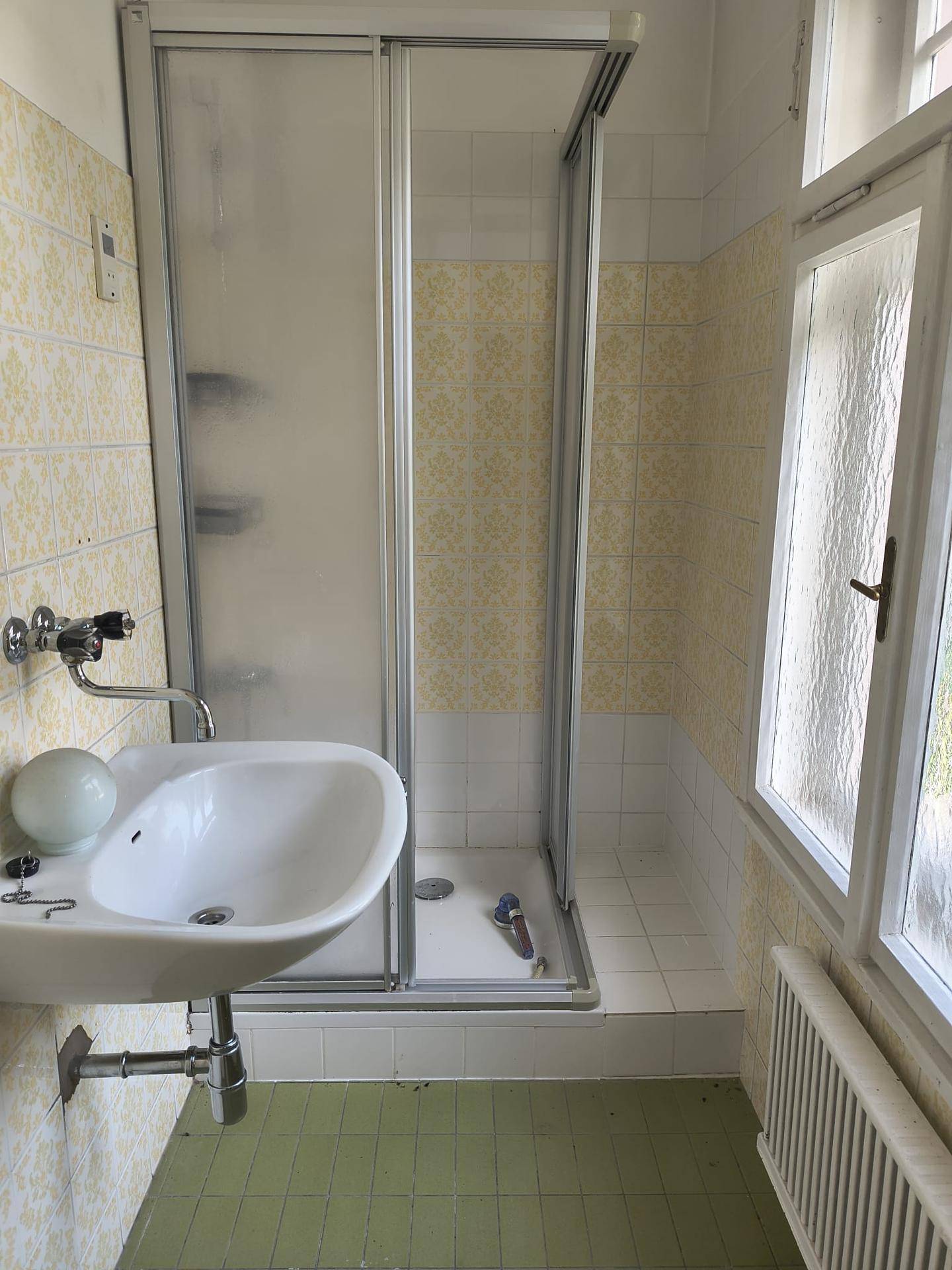 Funktionales Badezimmer mit Duschkabine, Waschbecken und Fenster, ausgestattet mit hellgrünen Fliesen.