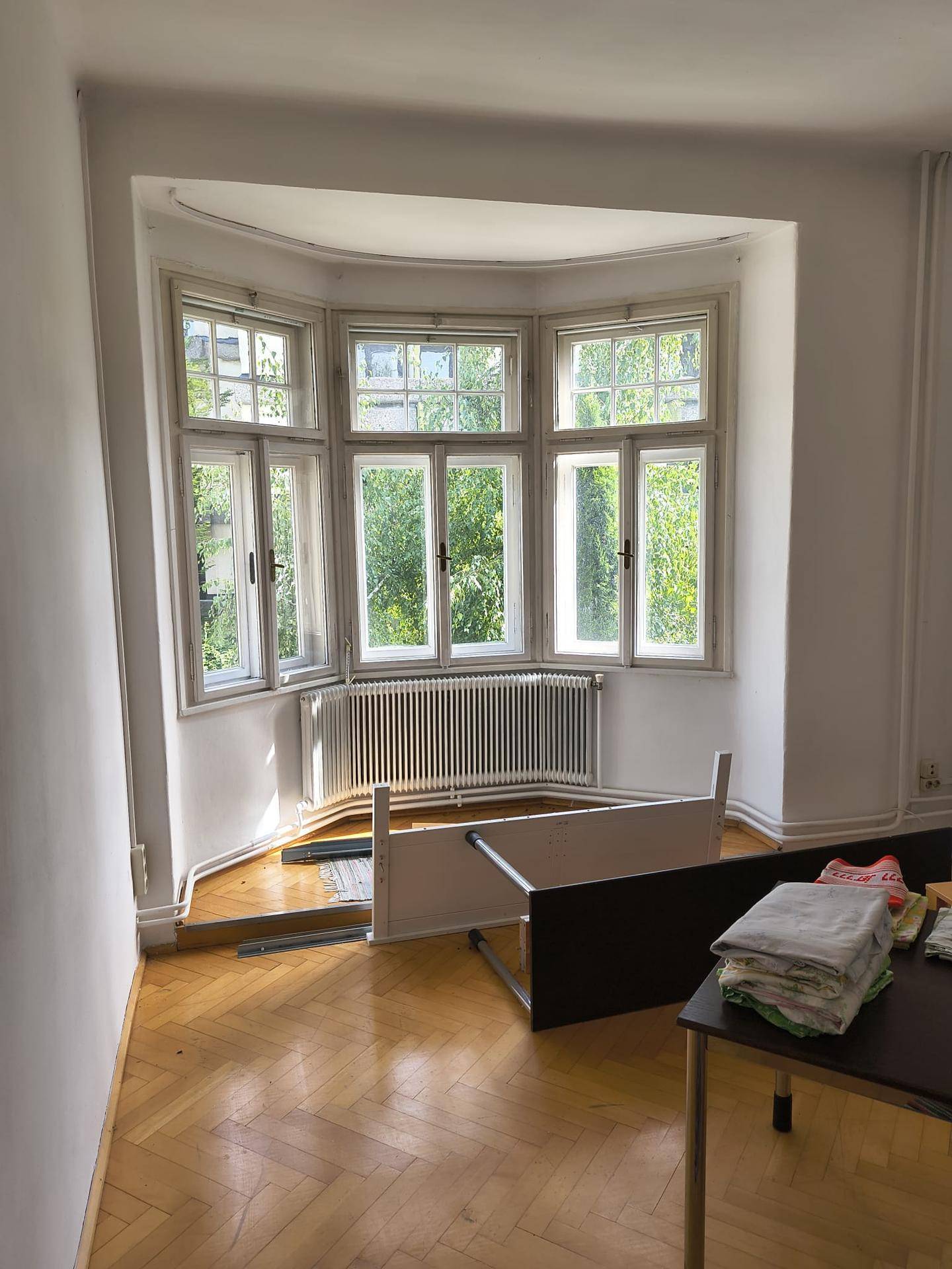 Heller Raum mit Fischgrätparkett und einem charmanten Erkerfenster, das viel Tageslicht hereinlässt.