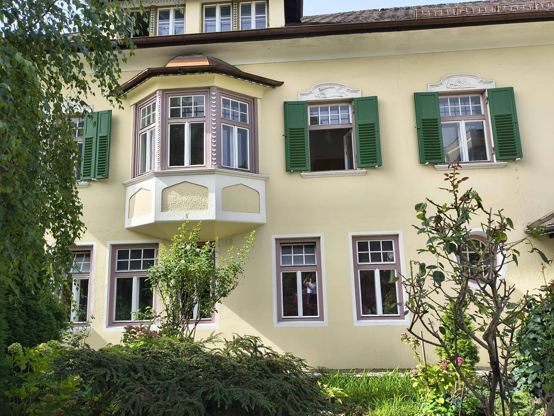 Historische Fassade mit gelbem Putz, grünen Fensterläden und einem markanten Erkerfenster.