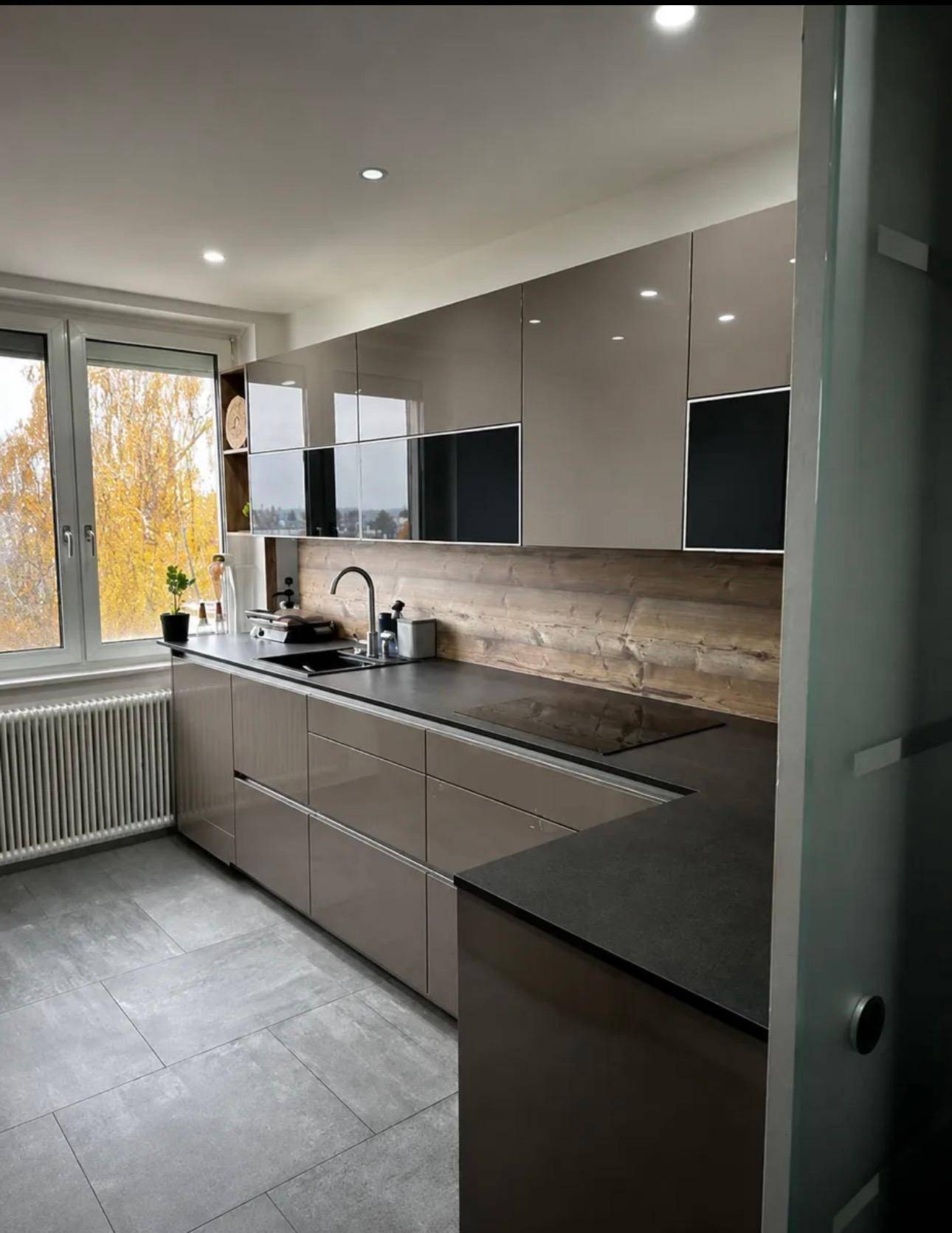 Helle moderne Küche mit Fenster, glänzenden Schränken und Holz-Akzenten.