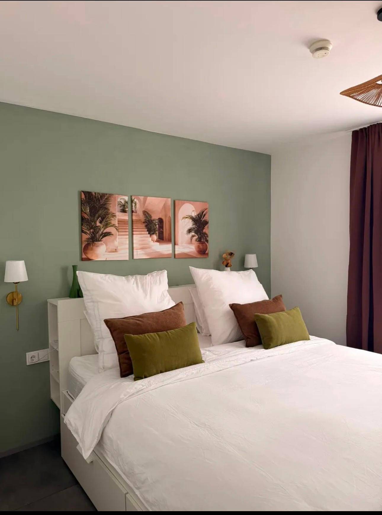Gemütliches Schlafzimmer mit grüner Akzentwand, Doppelbett und dekorativen Bildern.