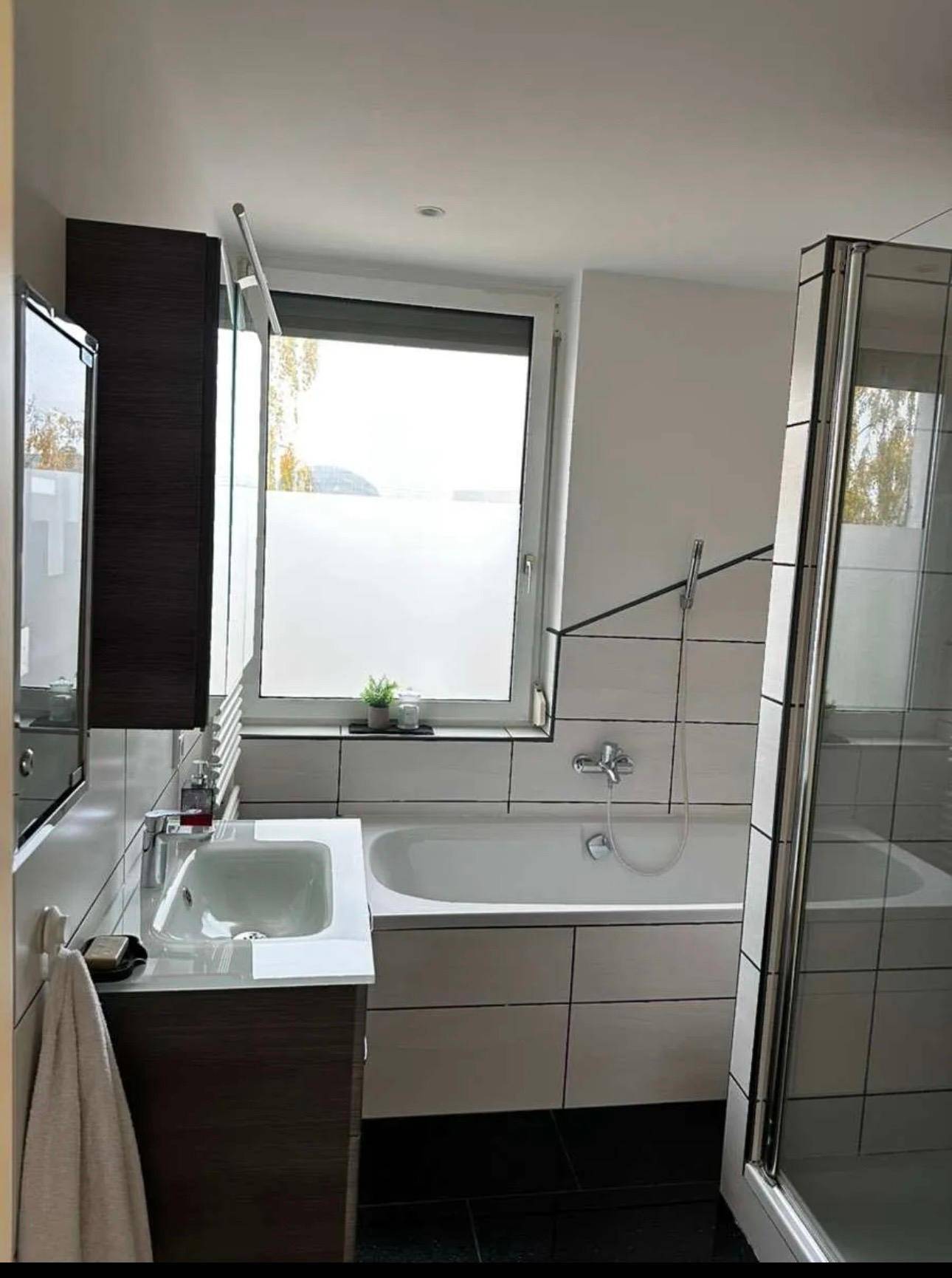 Modernes Badezimmer mit Badewanne, Duschkabine, Fenster und eleganten Fliesen.