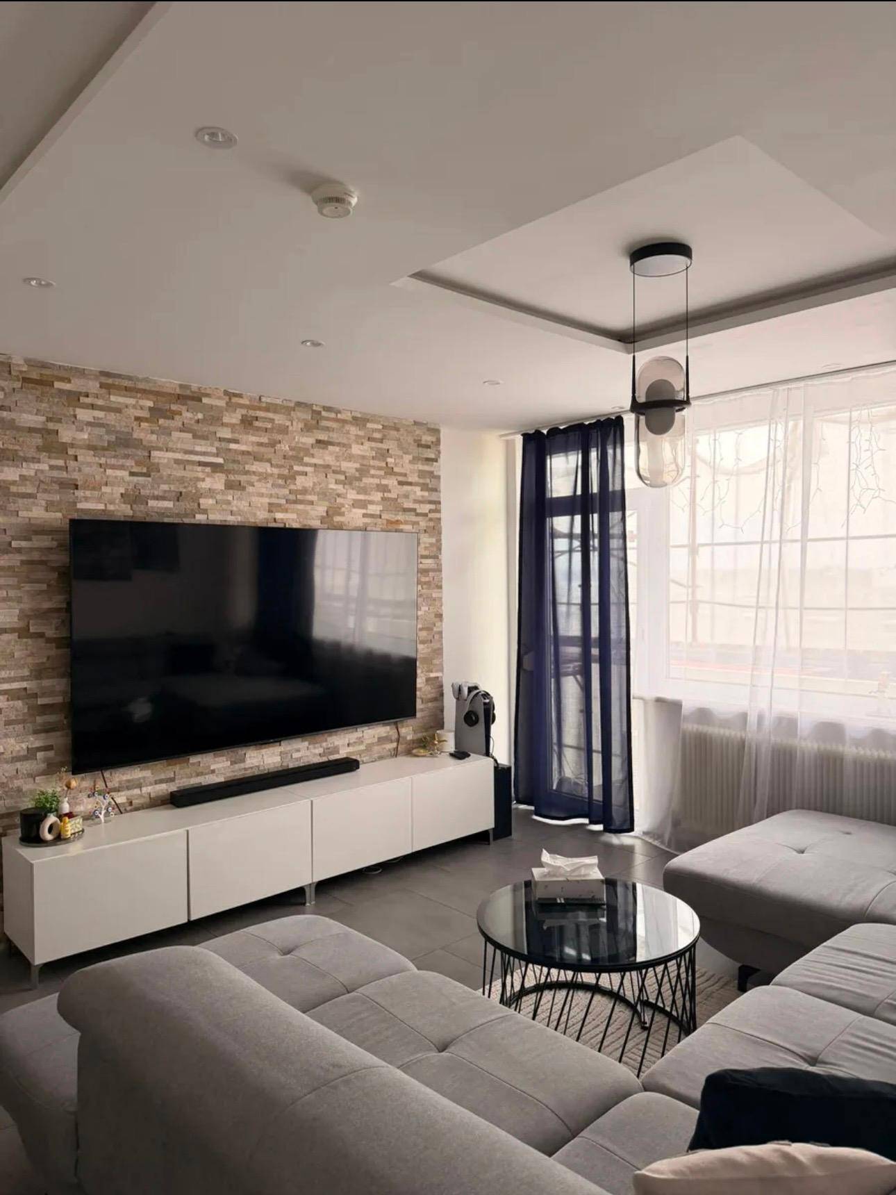 Gemütliches Wohnzimmer mit dekorativer Steinwand, großem Fernseher und moderner Beleuchtung.