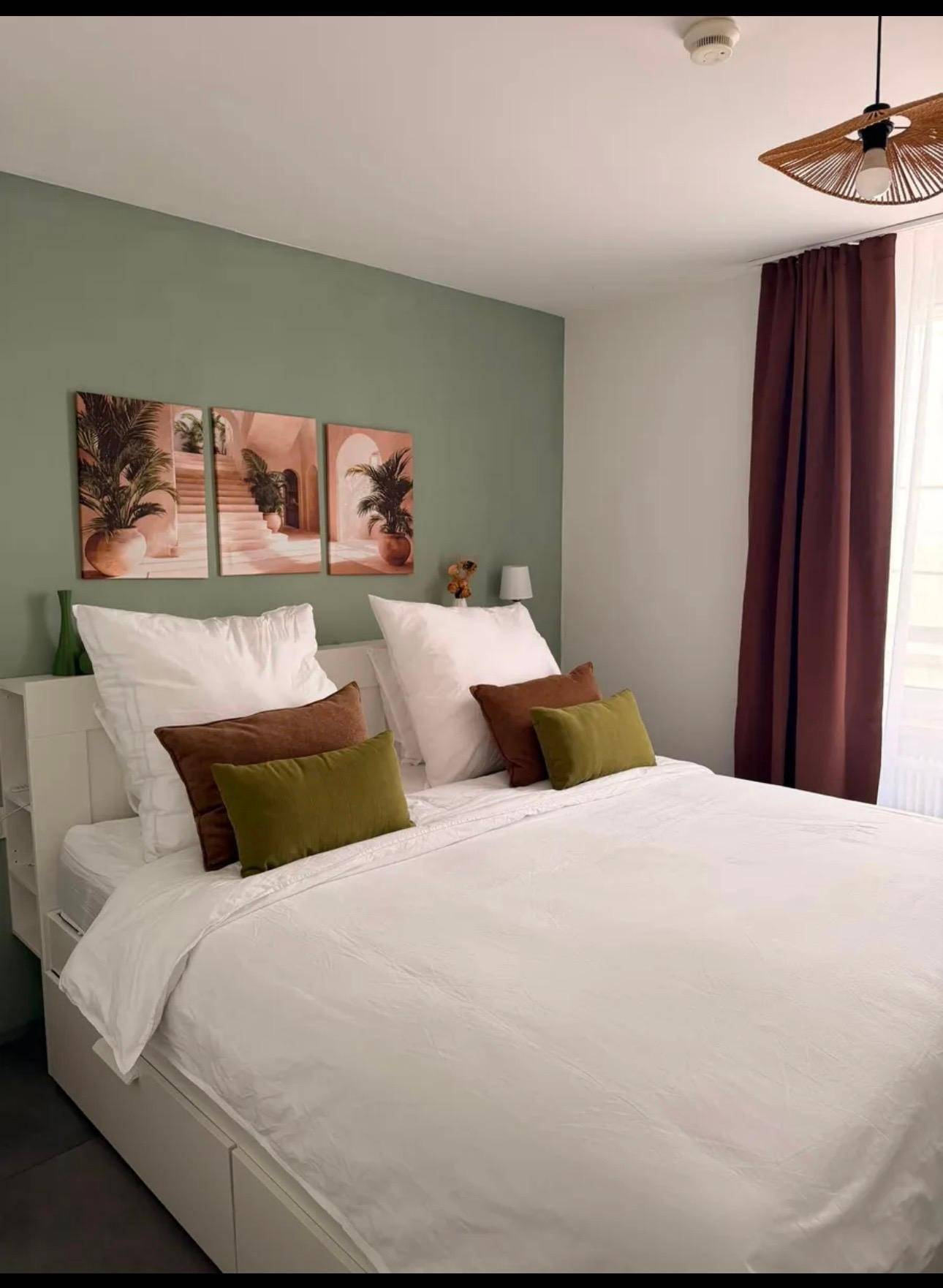 Helles Schlafzimmer mit grüner Wand, großem Bett und Vorhängen.