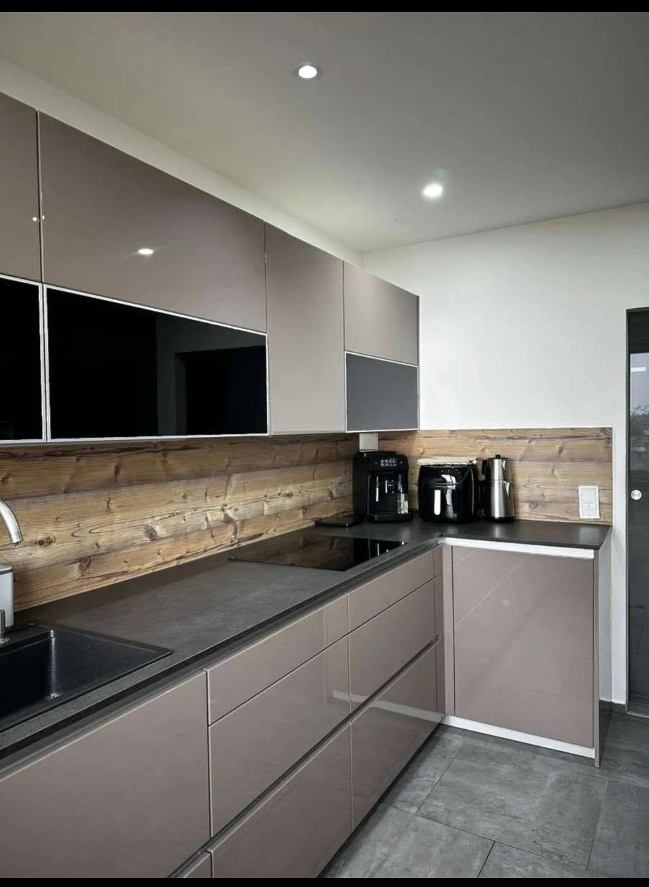 Moderne Küche mit glänzenden taupefarbenen Schränken, Holzrückwand und integrierten Geräten.