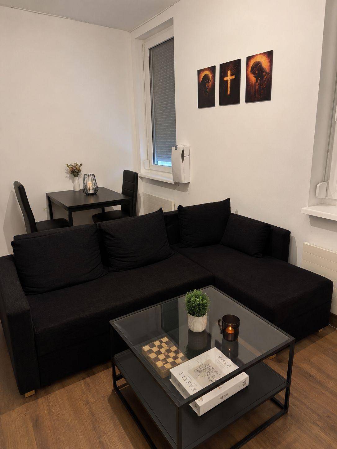 Gemütlicher Wohn- und Essbereich mit schwarzem Sofa, Couchtisch und kleinem Esstisch.