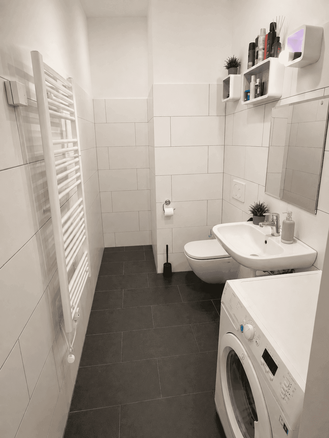 Modernes Badezimmer mit Waschmaschine, WC, Waschbecken und beheiztem Handtuchhalter.