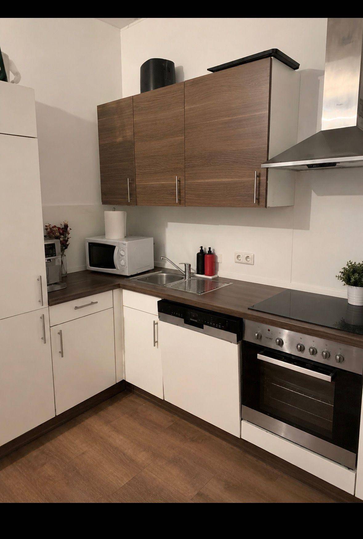 Funktionale Küche mit weißen und holzfarbenen Schränken, ausgestattet mit modernen Geräten.