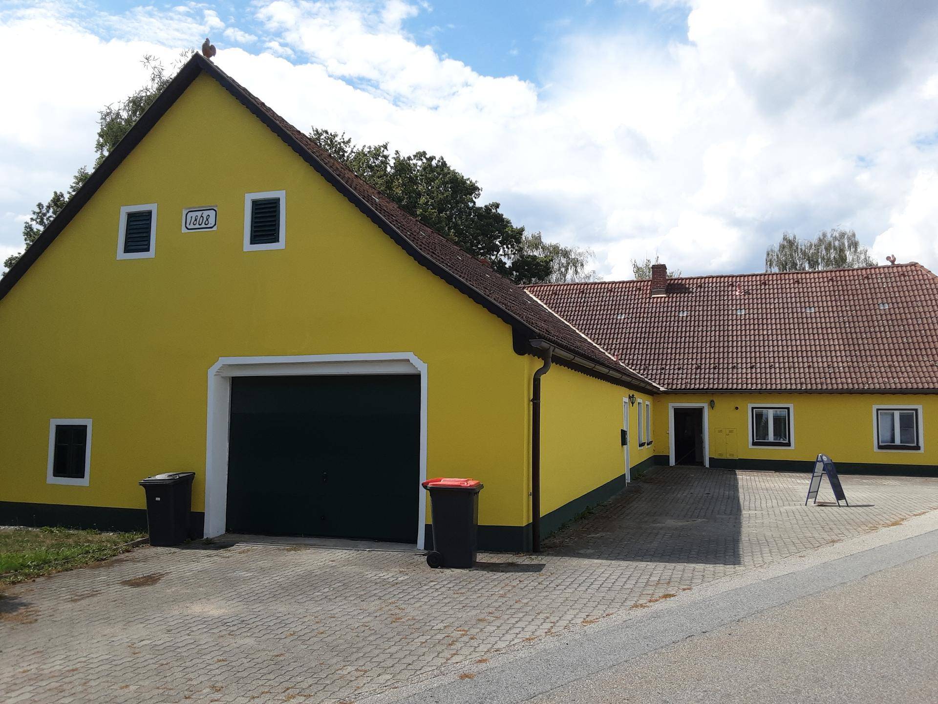 Rückansicht des gelben Landhauses mit großem Garagentor und traditioneller Jahreszahl über dem Eingang.