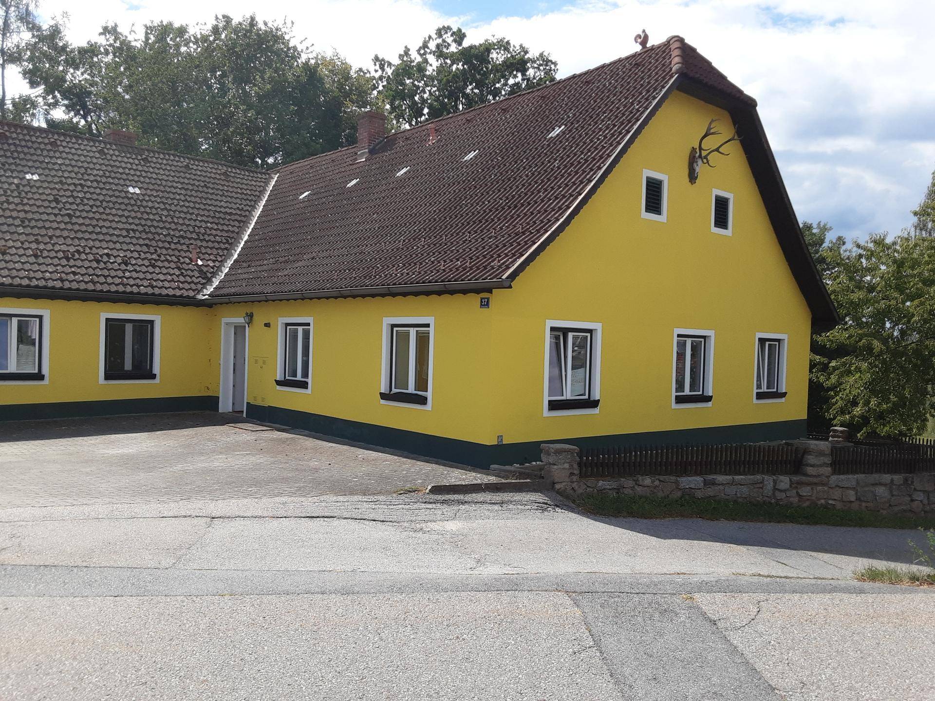 Charmantes gelbes Landhaus mit Ziegeldach und Hirschgeweih-Dekoration an der Giebelseite.