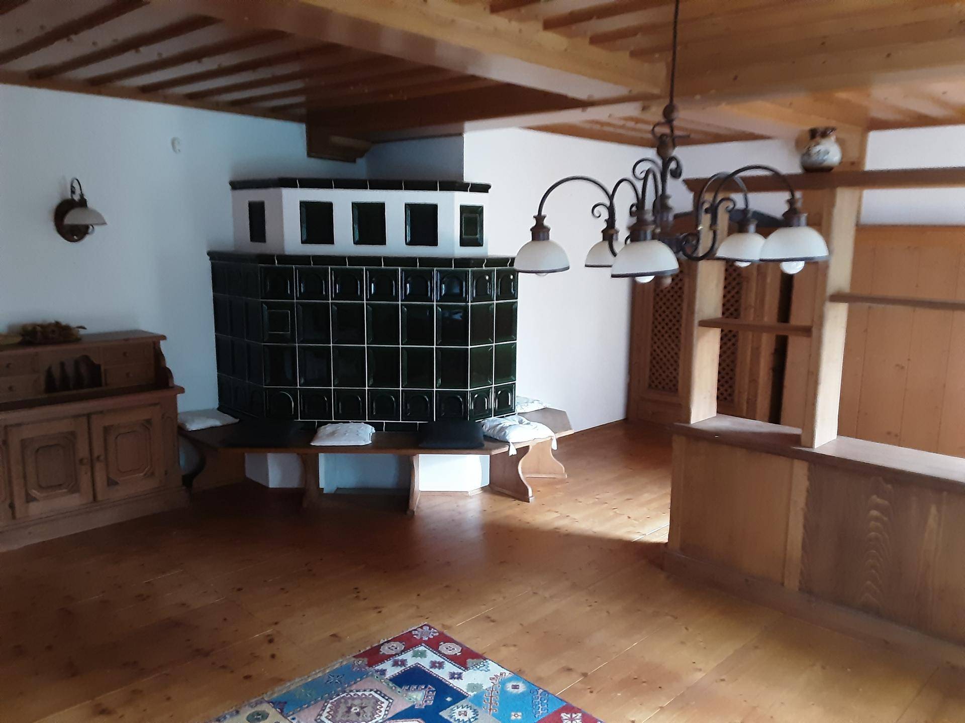 Geräumiges Wohnzimmer mit Holzbalkendecke, Parkettboden und einem großen Kachelofen als Blickfang.