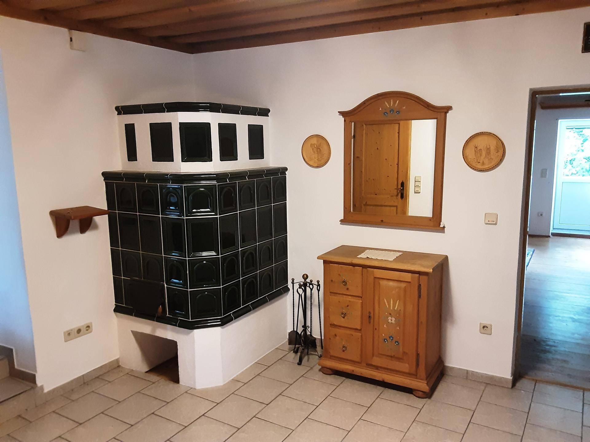 Eingangsbereich mit traditionellem Kachelofen, Holzmöbeln und Fliesenboden, der Gemütlichkeit ausstrahlt.