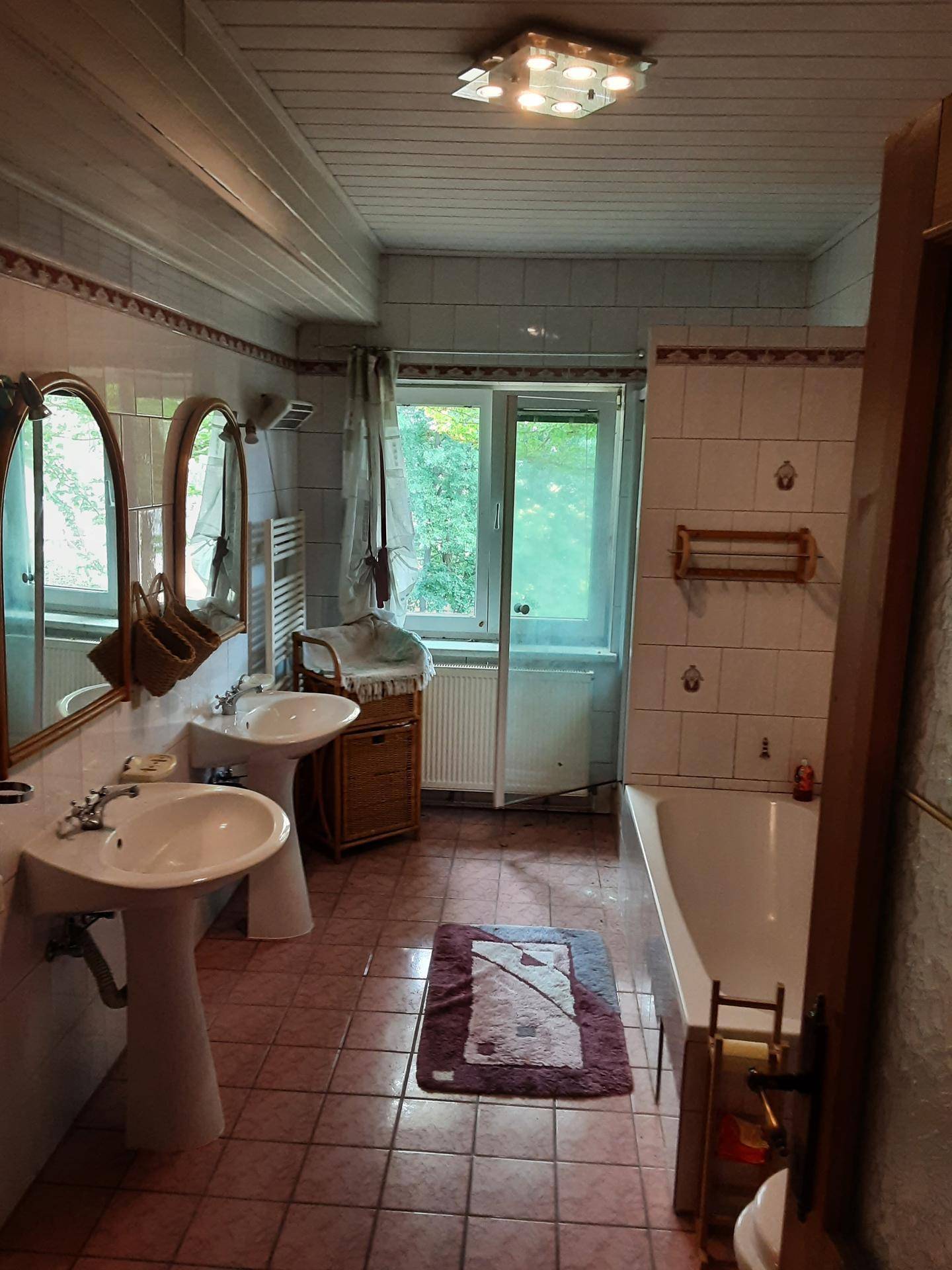 Badezimmer im 80er-Jahre-Stil mit rosa Fliesen, zwei Waschbecken und einer Badewanne.