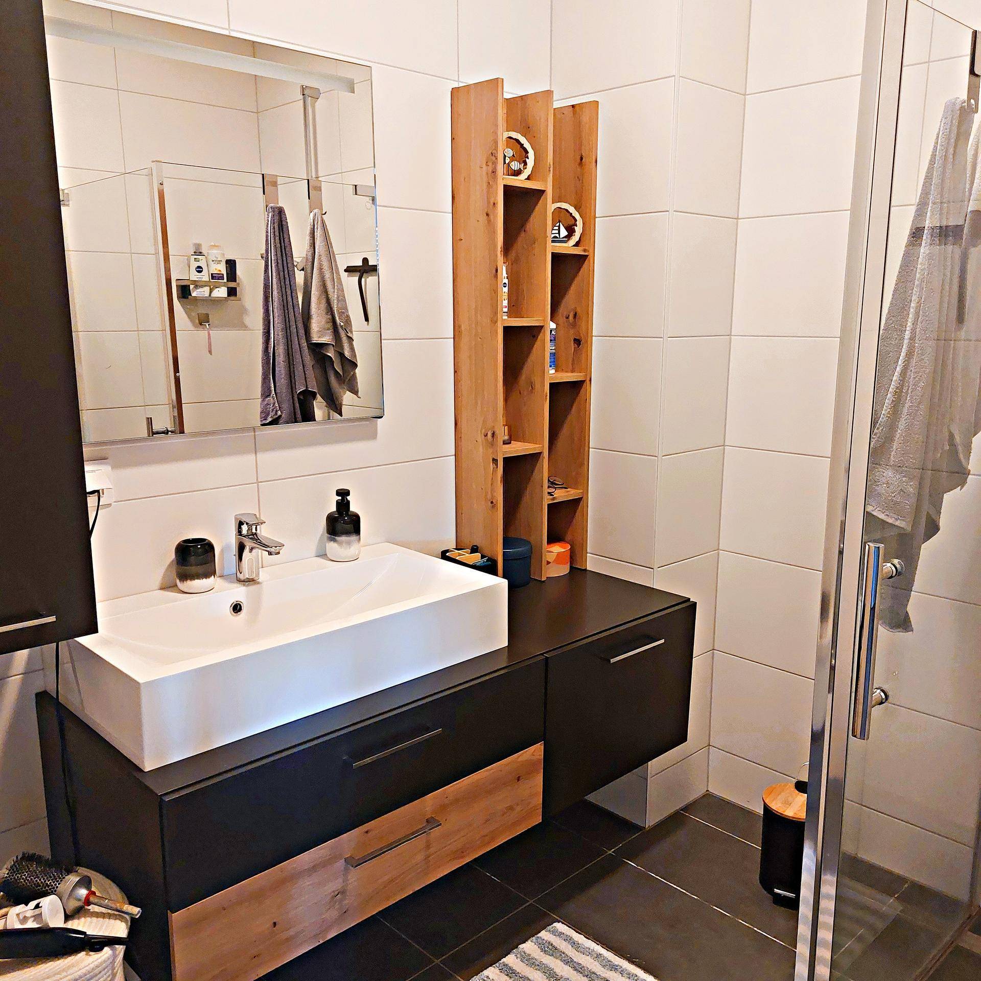Modernes Badezimmer mit weiß gefliesten Wänden, dunklem Boden und begehbarer Dusche.
