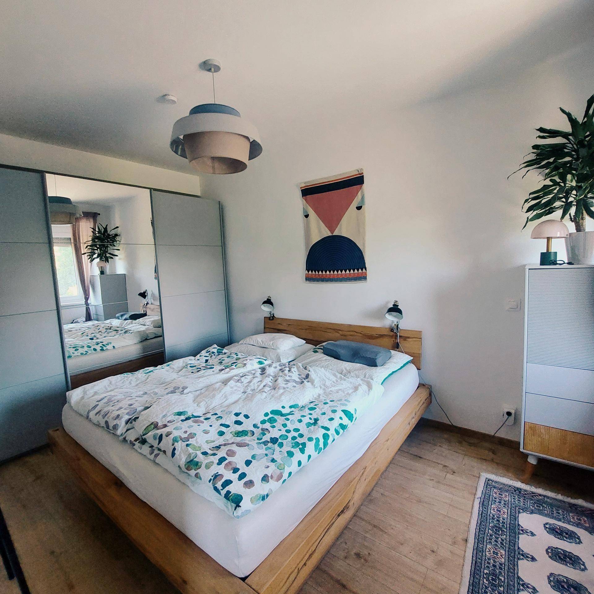 Helles Schlafzimmer mit Holzbett, Spiegelschrank und minimalistischer Dekoration.