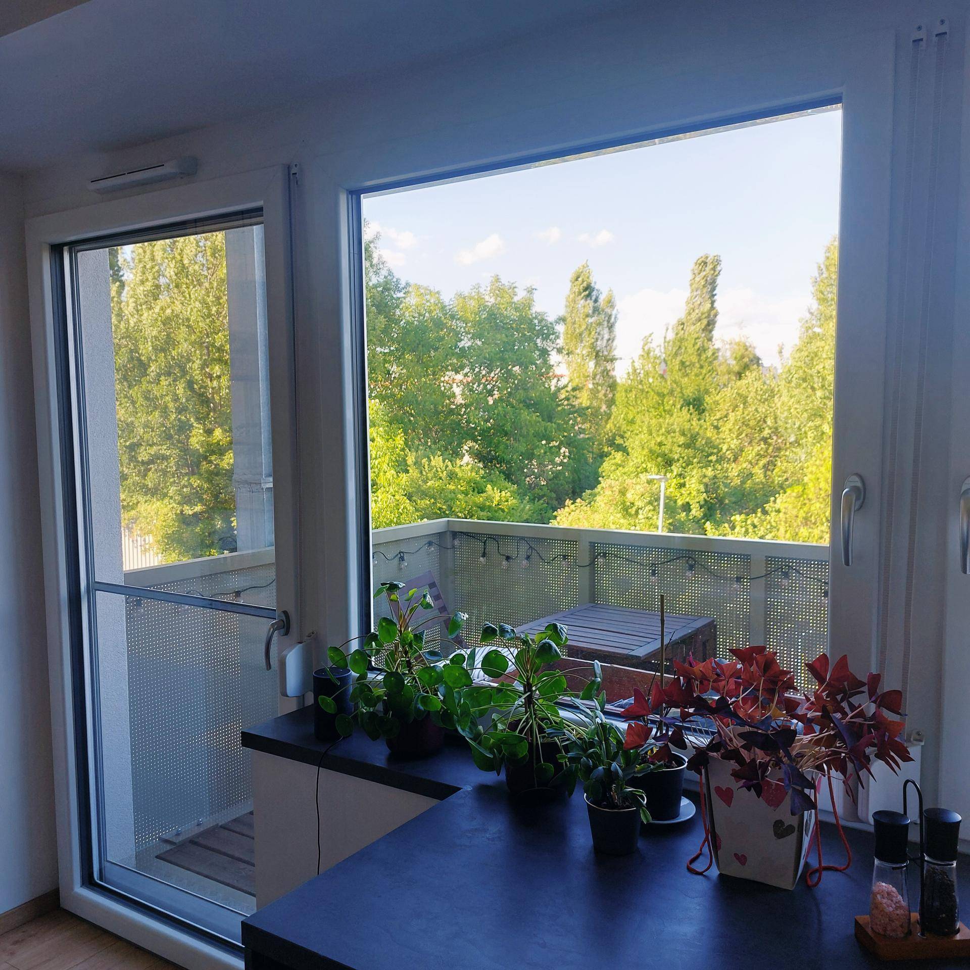 Blick vom Innenraum auf einen möblierten Balkon mit üppiger grüner Aussicht.