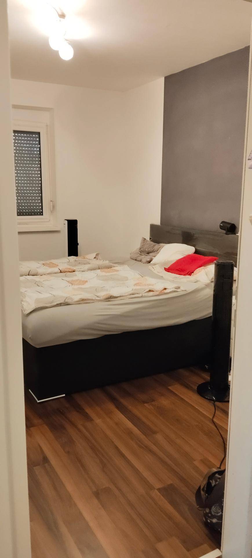 Schlafzimmer mit Doppelbett, Holzfußboden und einem Fenster mit Rollladen.