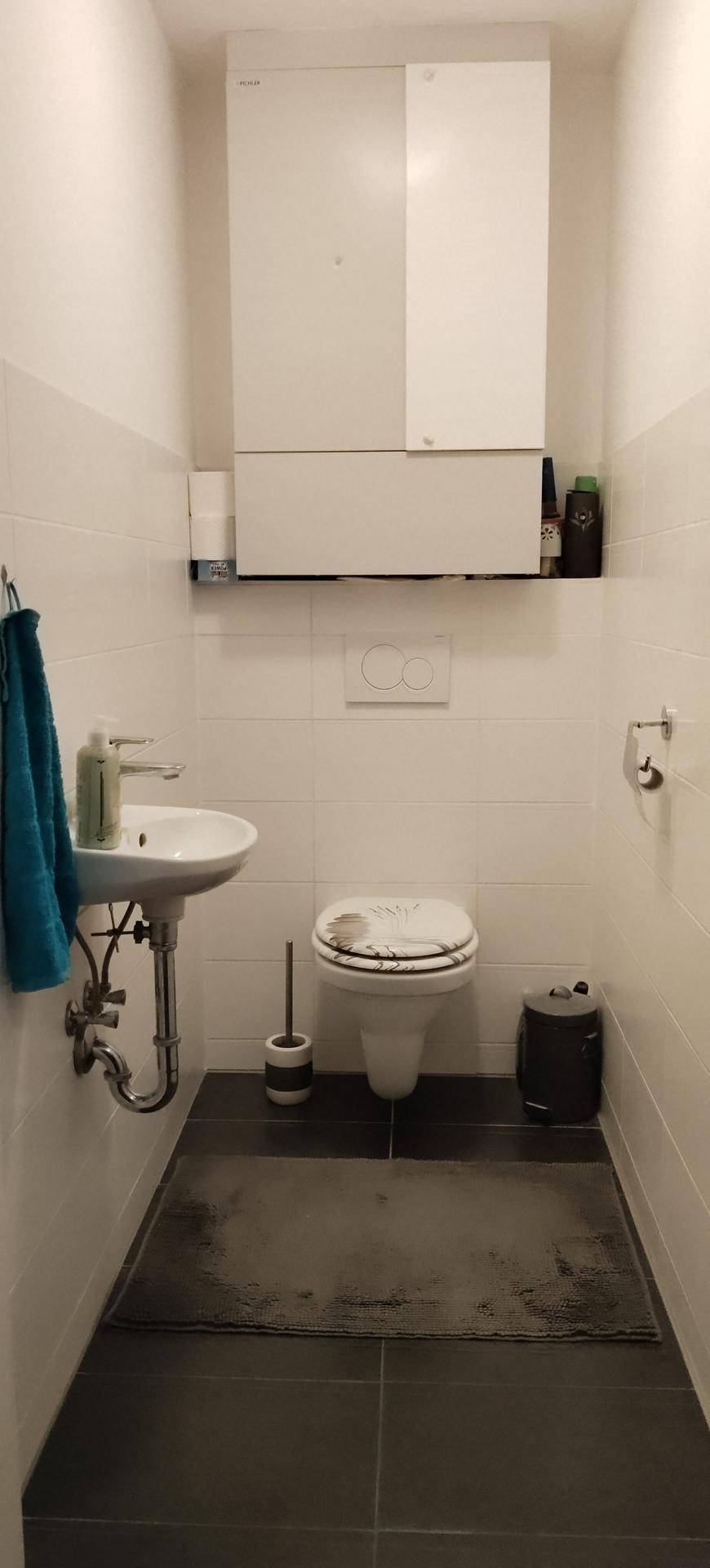 Kleines Gäste-WC mit Wand-WC, Waschbecken und weißen Fliesen an den Wänden.