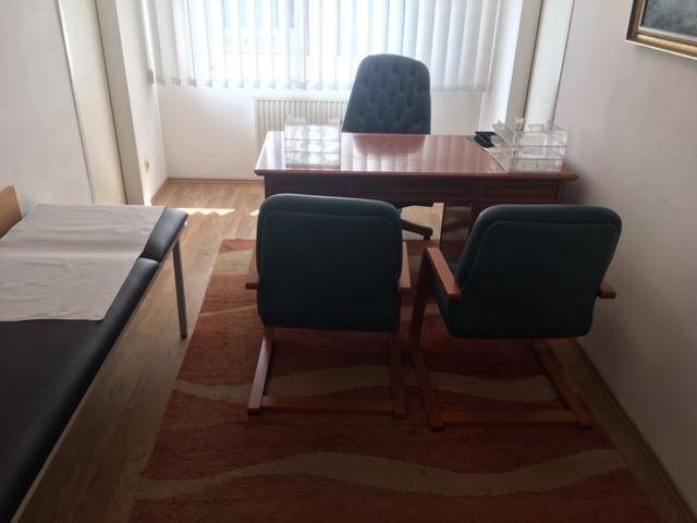 Arbeitszimmer mit Schreibtisch, Stühlen, Untersuchungsliege und Teppichboden.