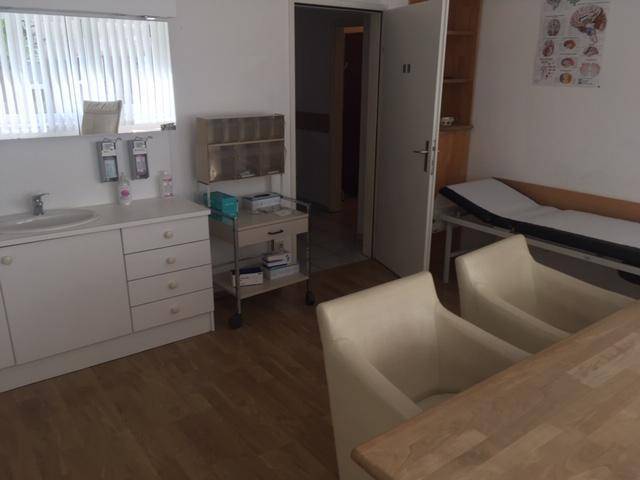 Behandlungszimmer mit Waschbecken, Unterschränken und Untersuchungsliege.