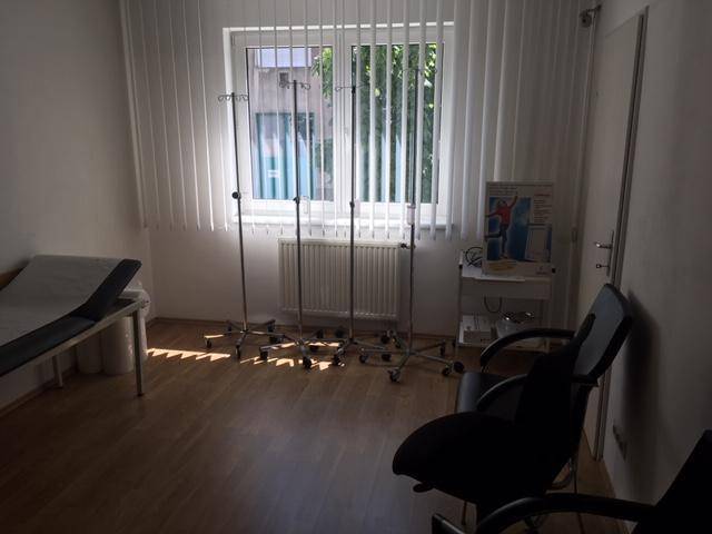 Behandlungszimmer mit Untersuchungsliege, Infusionsständern und Fenster.