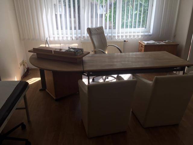 Helles Büro mit großem Schreibtisch, bequemen Stühlen und Fenster mit Jalousien.