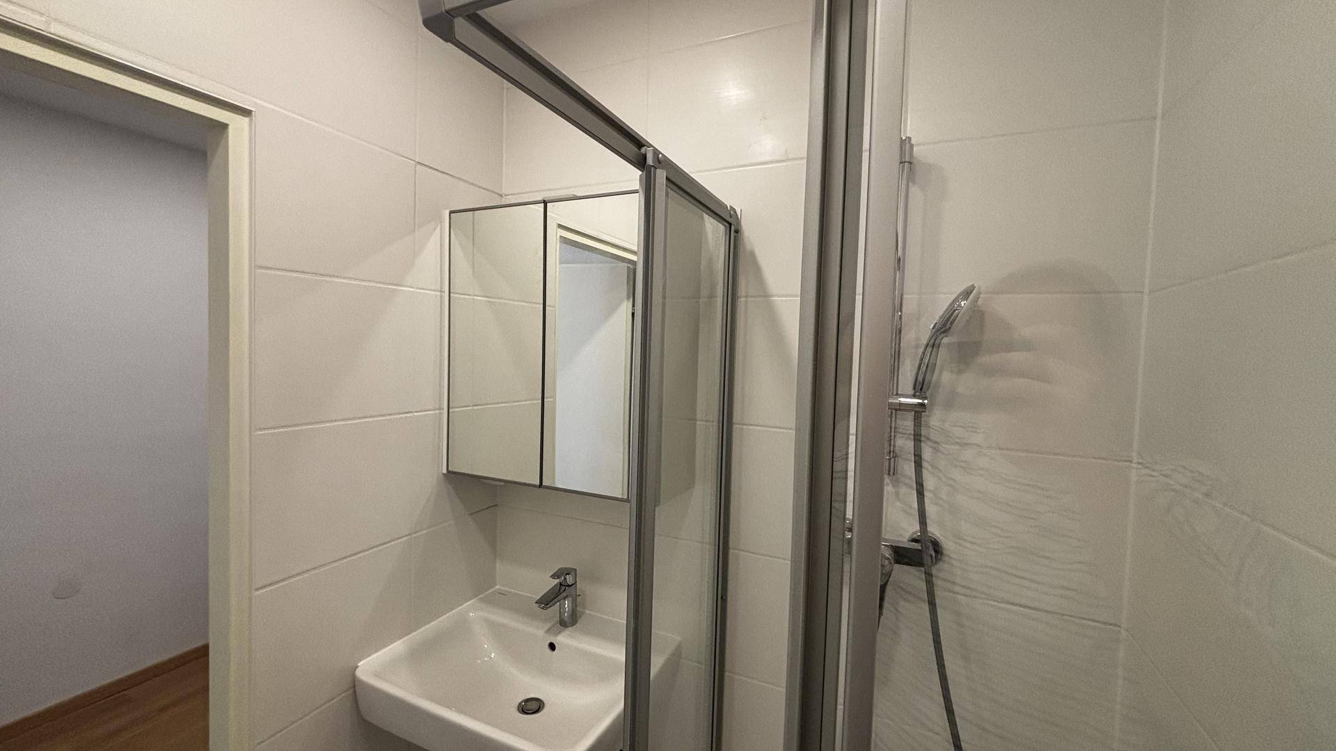 Modernes Badezimmer mit Duschkabine, Waschbecken und Spiegelschrank, komplett gefliest in Weiß.