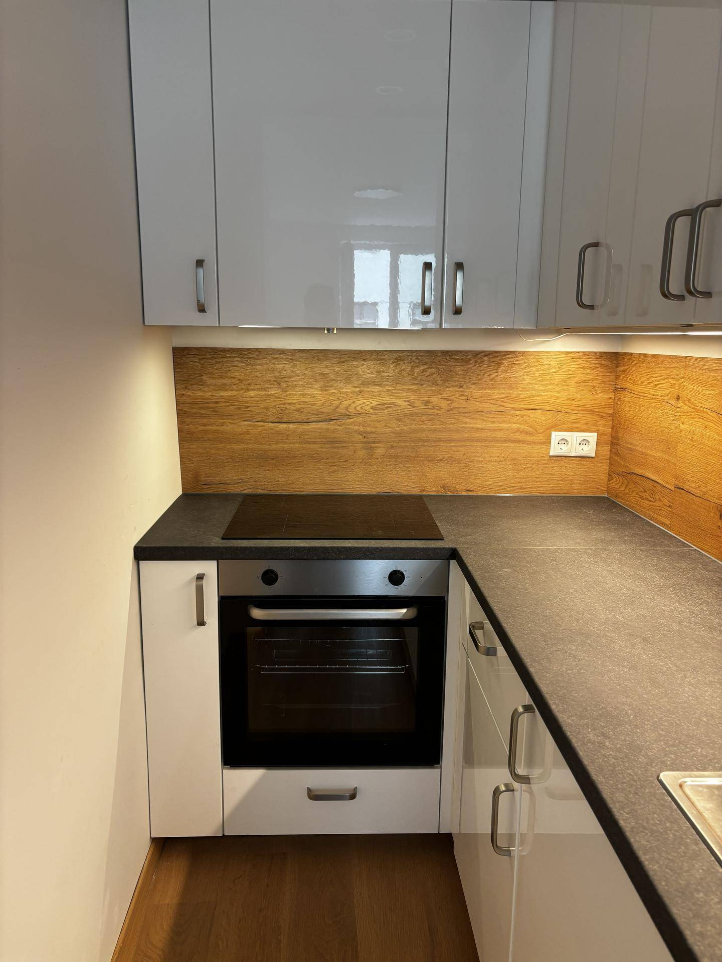 Moderne Küchenzeile mit Induktionskochfeld, Backofen, Spüle und weißen Hochglanzschränken.