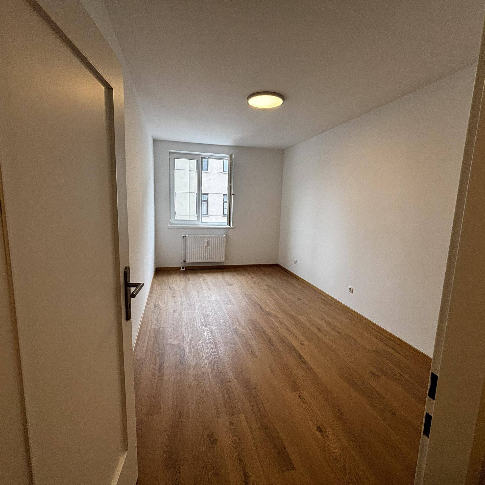 Helles, leeres Zimmer mit Holzboden und Fenster, bereit zur individuellen Gestaltung.