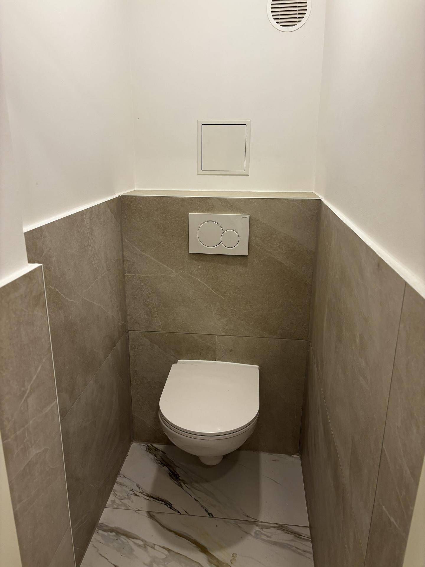Separates WC mit wandhängender Toilette und modernen Fliesen an Wänden und Boden.