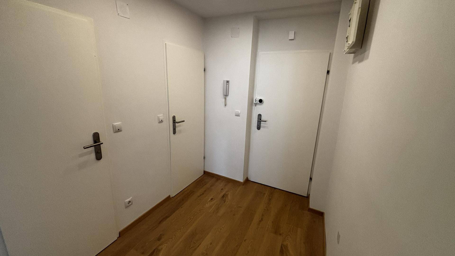 Heller Flur mit mehreren weißen Türen und einer Gegensprechanlage.