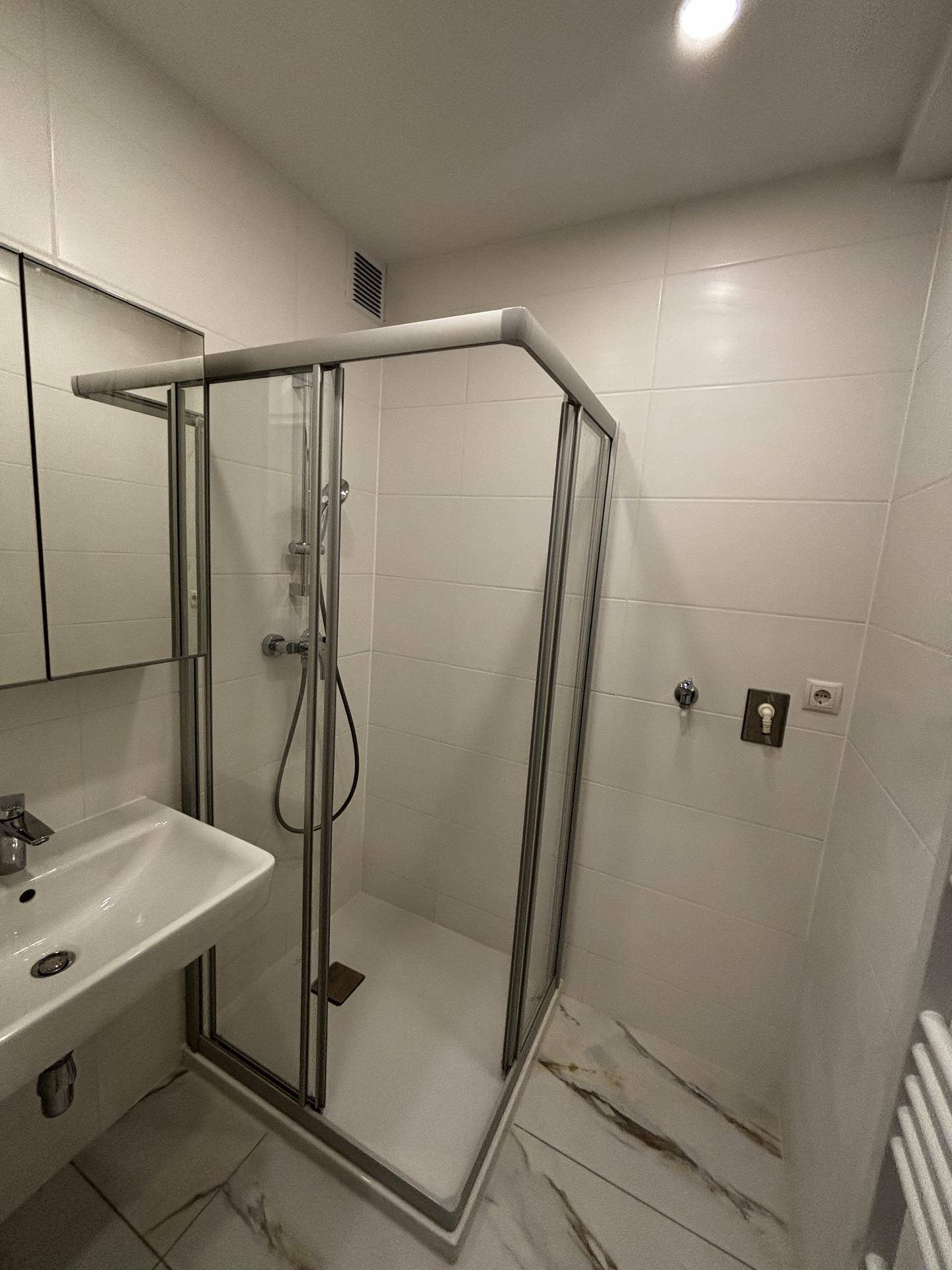Helles Badezimmer mit Duschkabine, Waschbecken, Spiegelschrank und beheiztem Handtuchhalter.