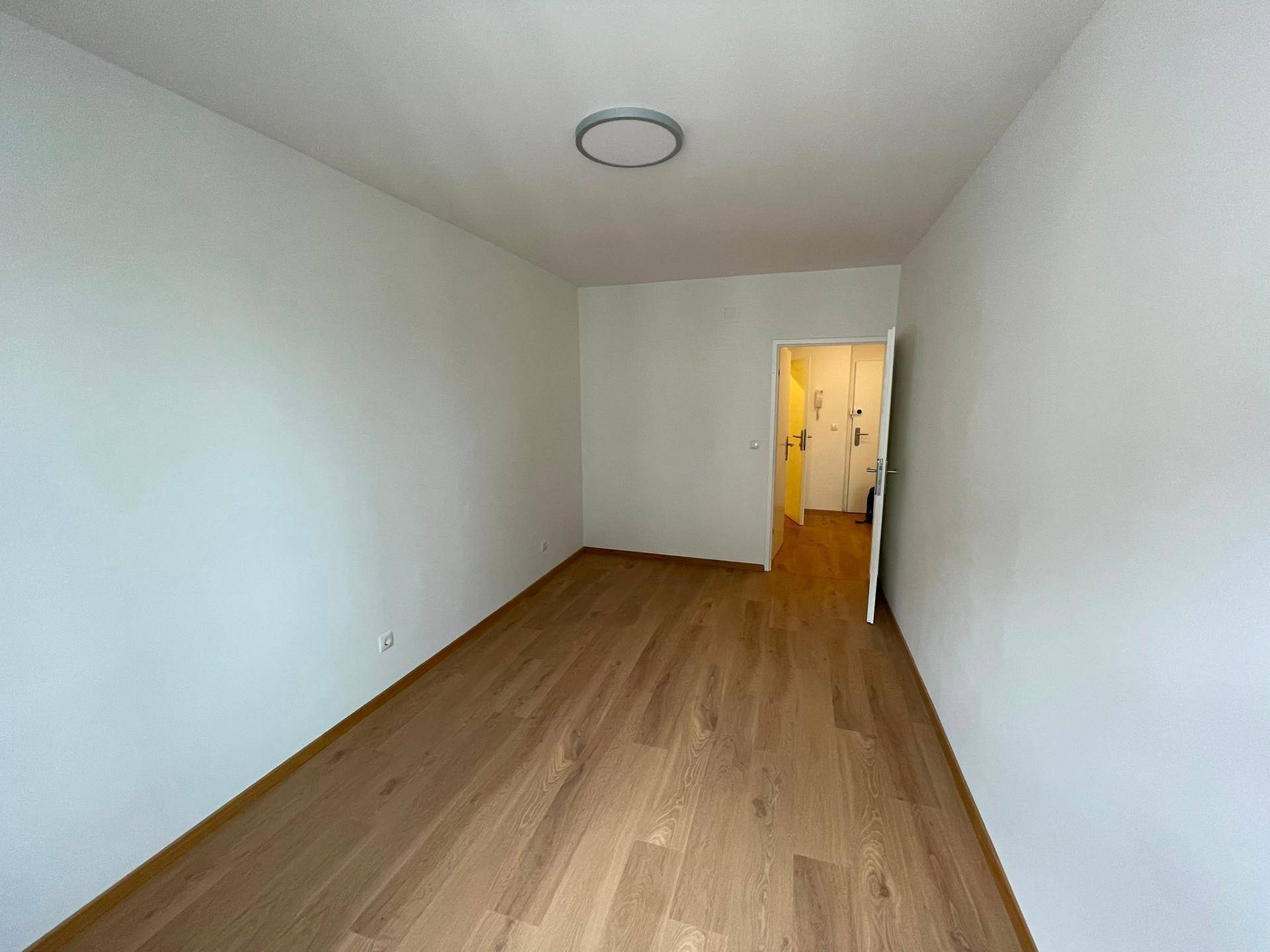 Lichtdurchflutetes Zimmer mit Holzboden und Zugang zu einem Flur, ideal für flexible Nutzung.