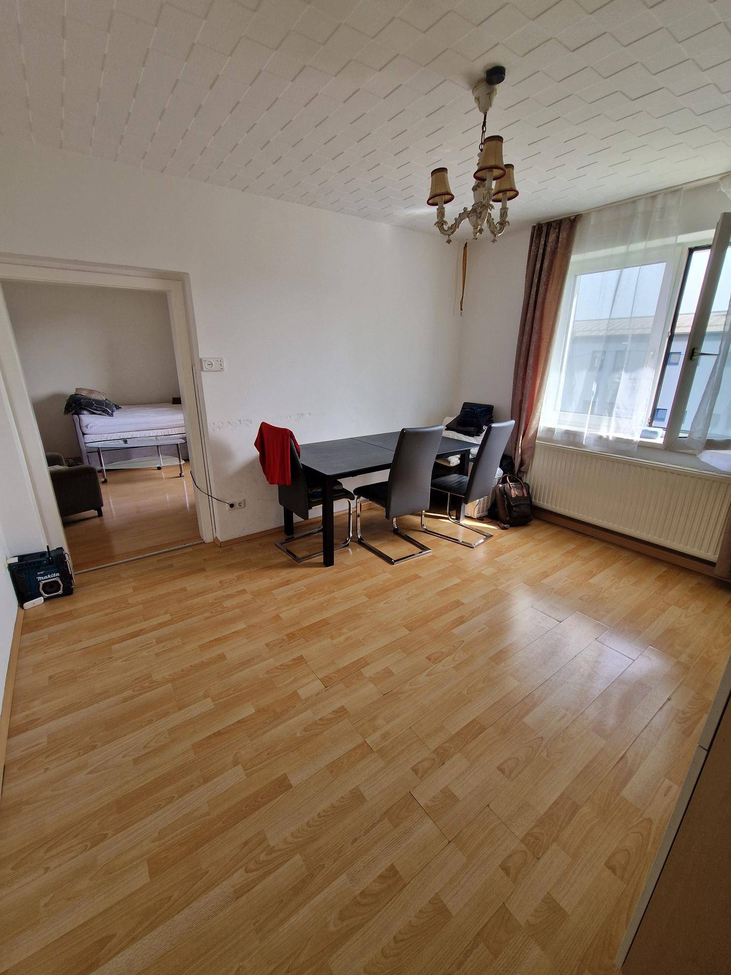 Essbereich mit dunklem Tisch und Stühlen, Laminatboden und offenem Zugang zu einem Schlafzimmer.
