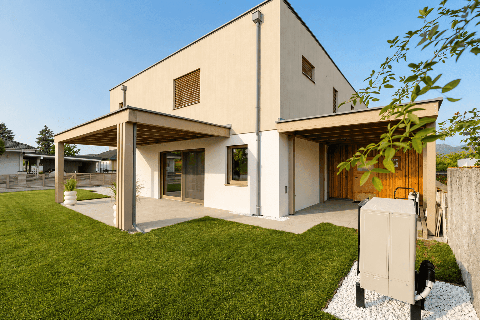 Rückansicht des modernen Hauses mit überdachter Terrasse, Rasenfläche und Wärmepumpe.