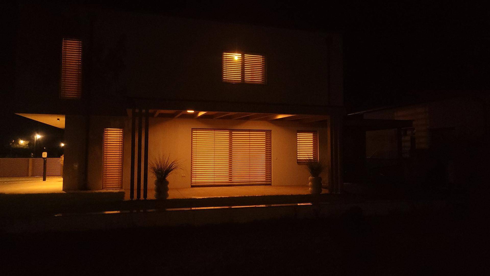 Das moderne Haus bei Nacht mit beleuchteten Fenstern und geschlossenen Jalousien.