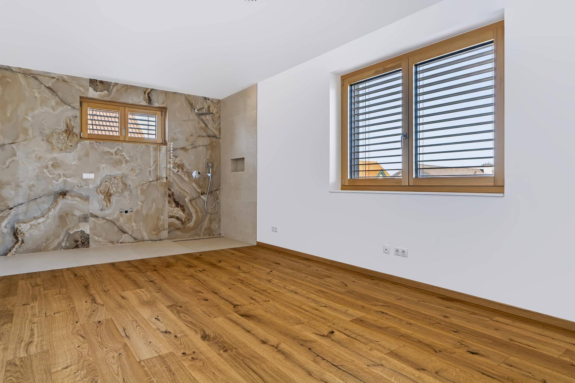 Geräumiges Schlafzimmer mit integriertem Badbereich, Holzboden und großen Fenstern.