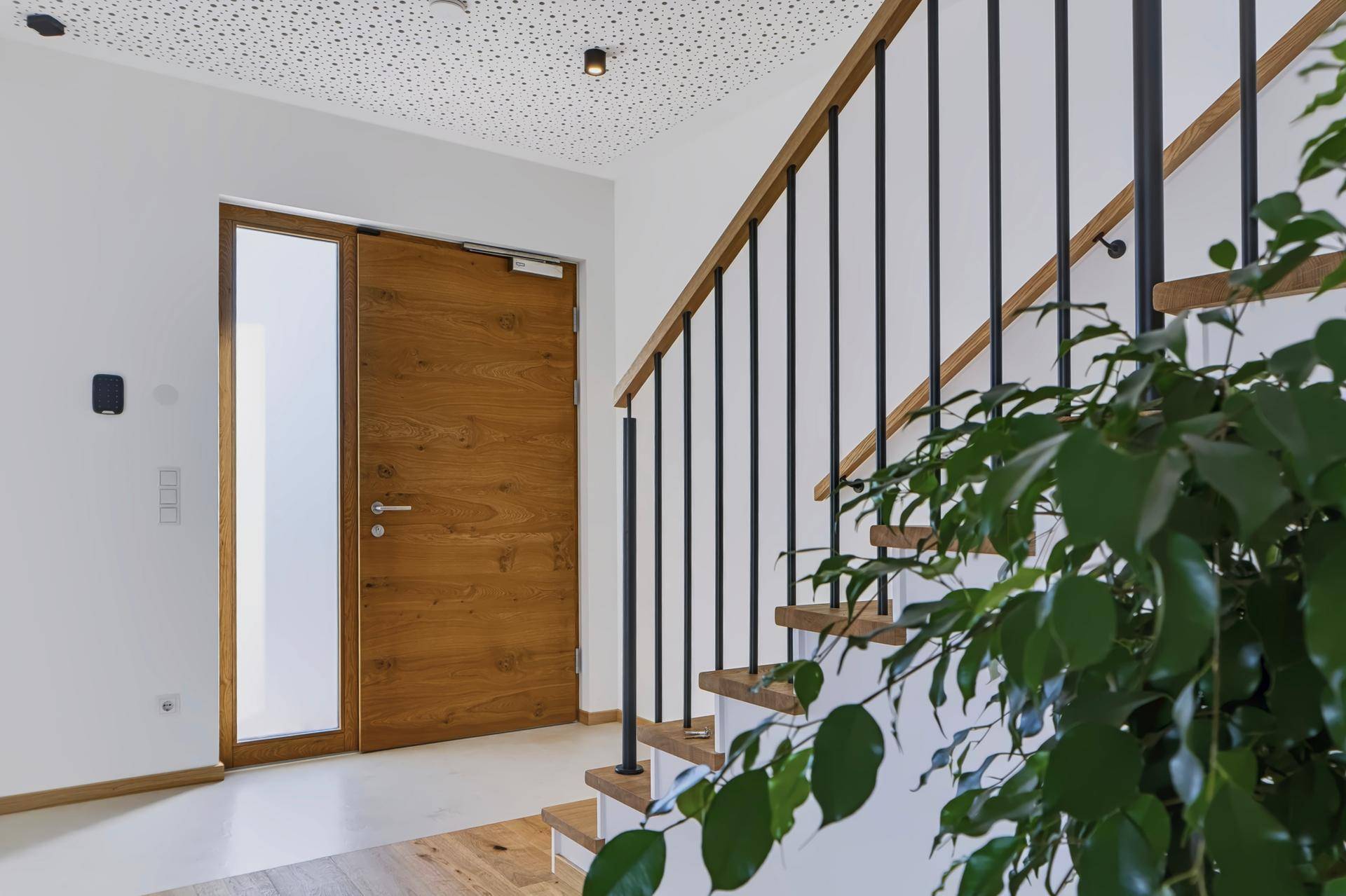 Heller Eingangsbereich mit moderner Holztür, Treppe und Blick auf das obere Stockwerk.