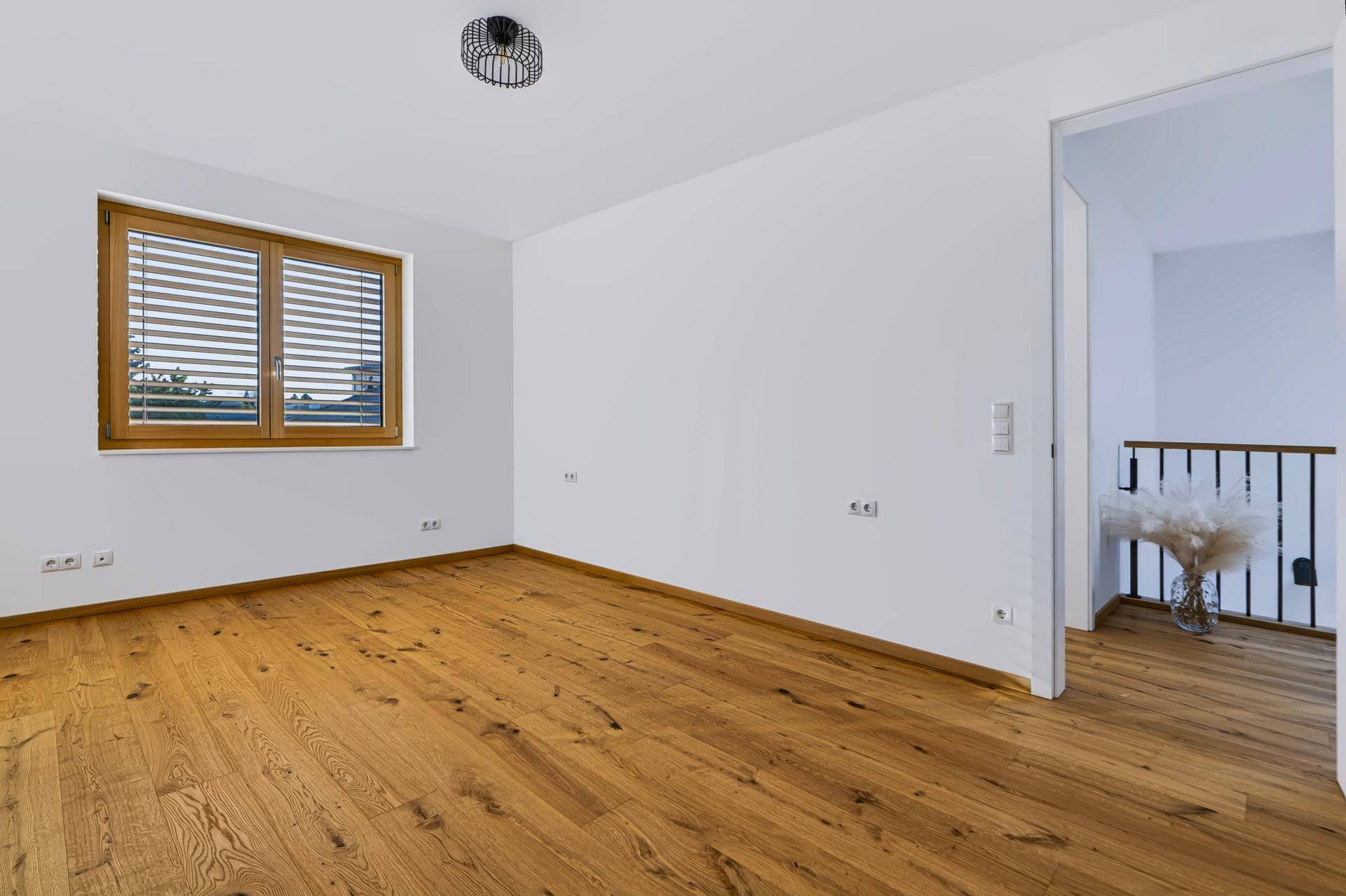 Helles Schlafzimmer mit Holzboden und Fenster mit Jalousien, bietet viel Tageslicht.