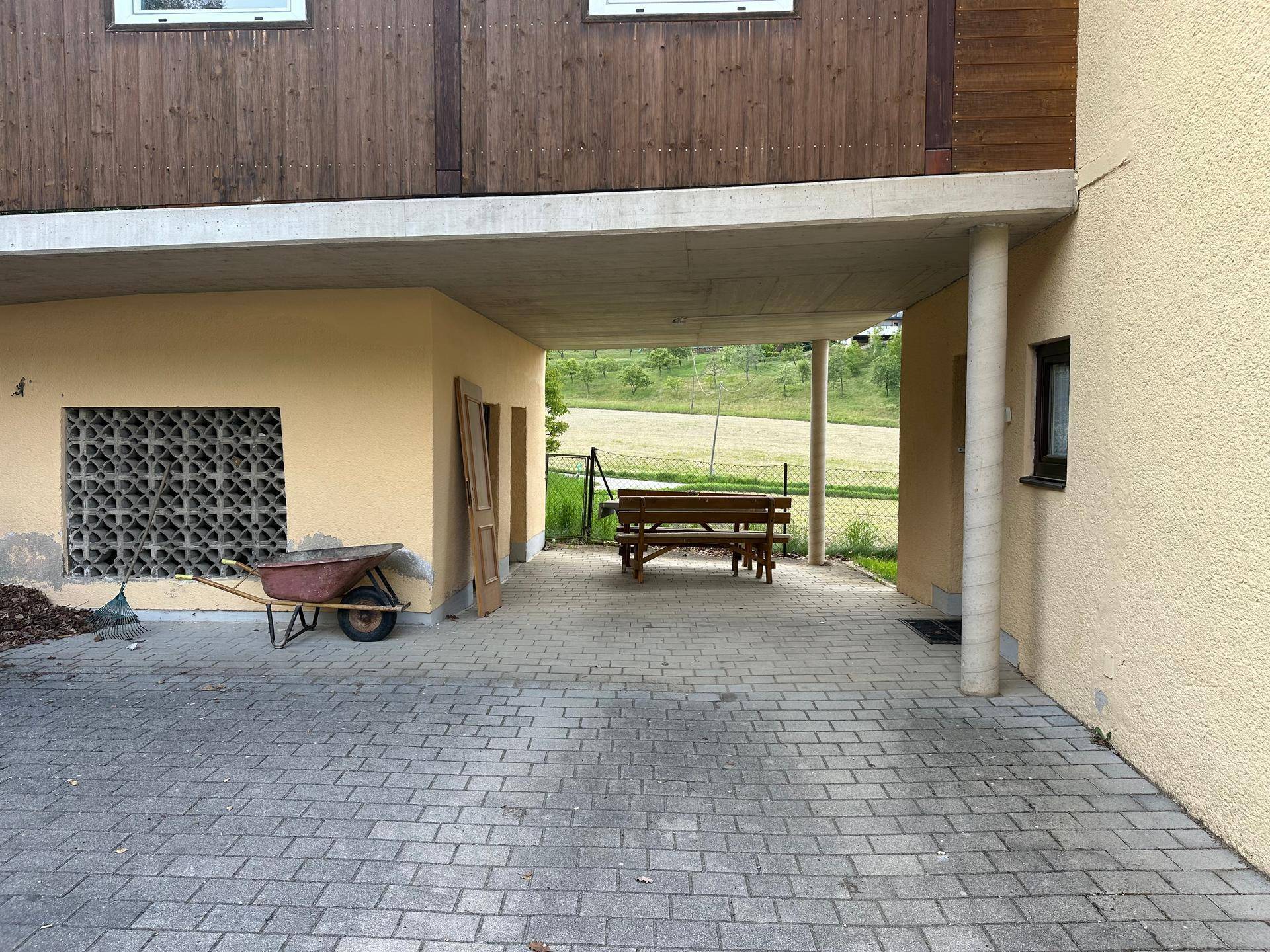 Überdachter Außenbereich mit gepflastertem Boden und einer Holzbank, ideal für Schatten.