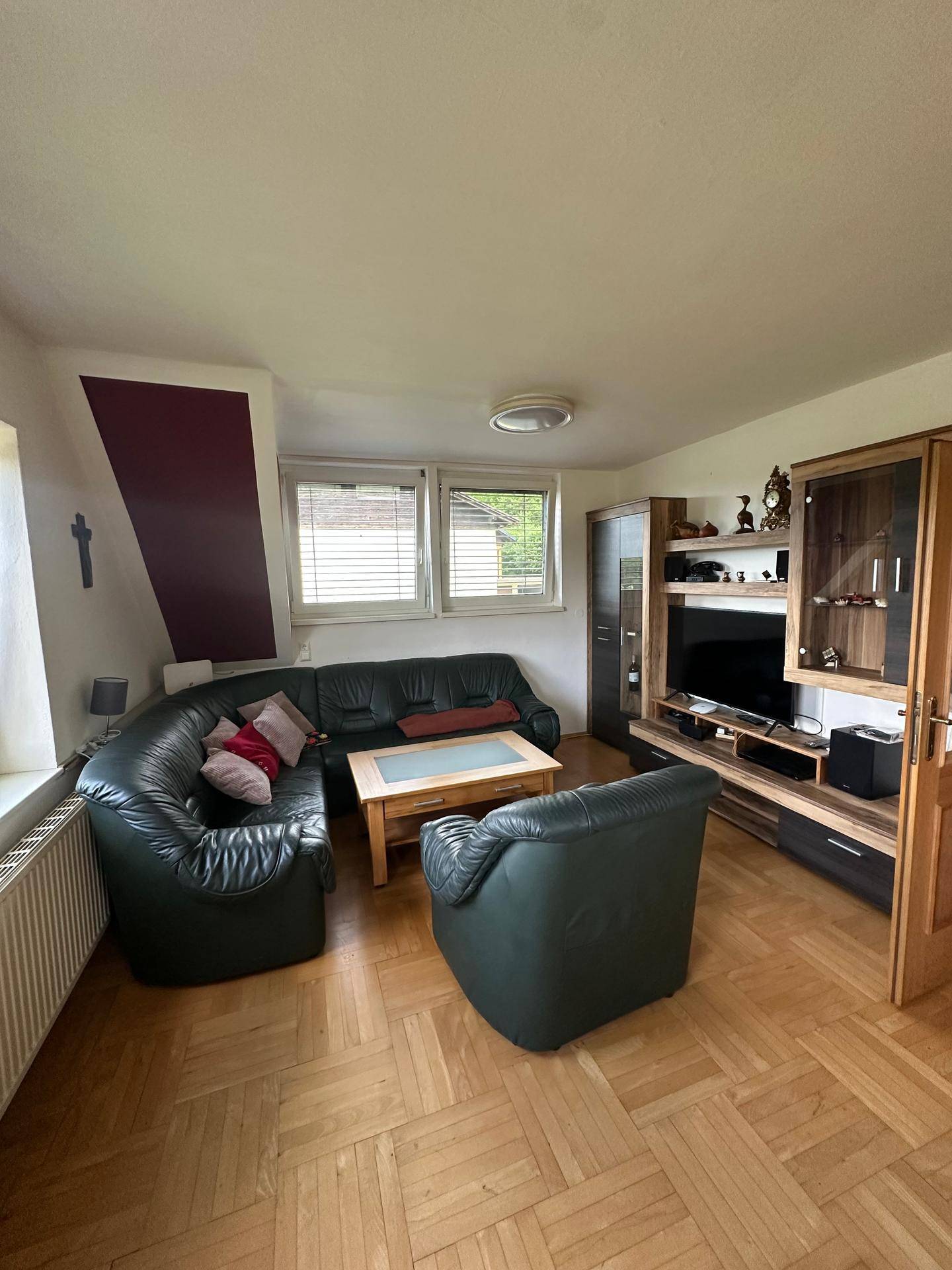 Geräumiges Wohnzimmer mit dunkler Ledercouch, Holzboden und Blick ins Grüne.