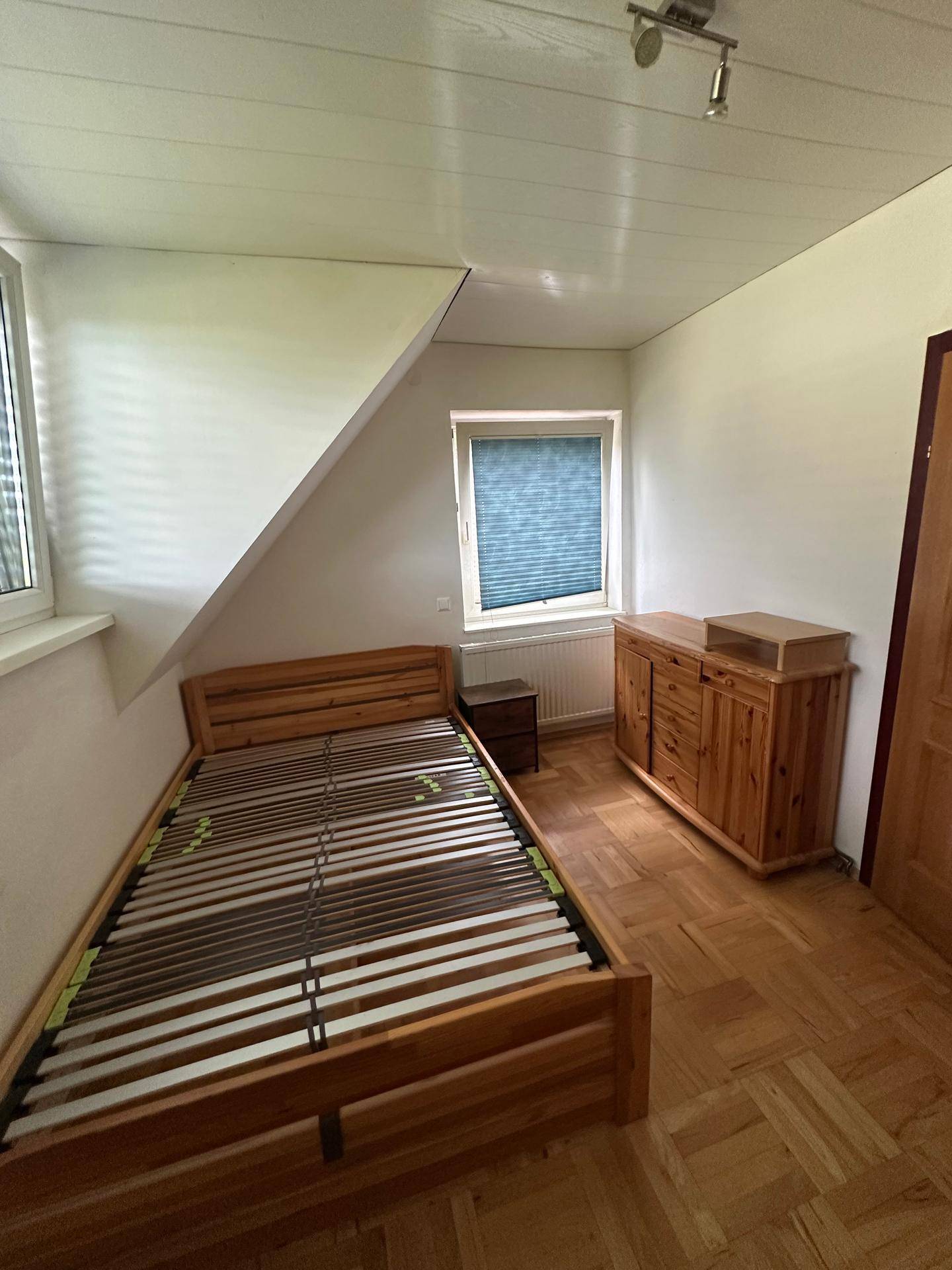Gemütliches Schlafzimmer mit Holzbett, Kommode und Dachschräge, hell und einladend.