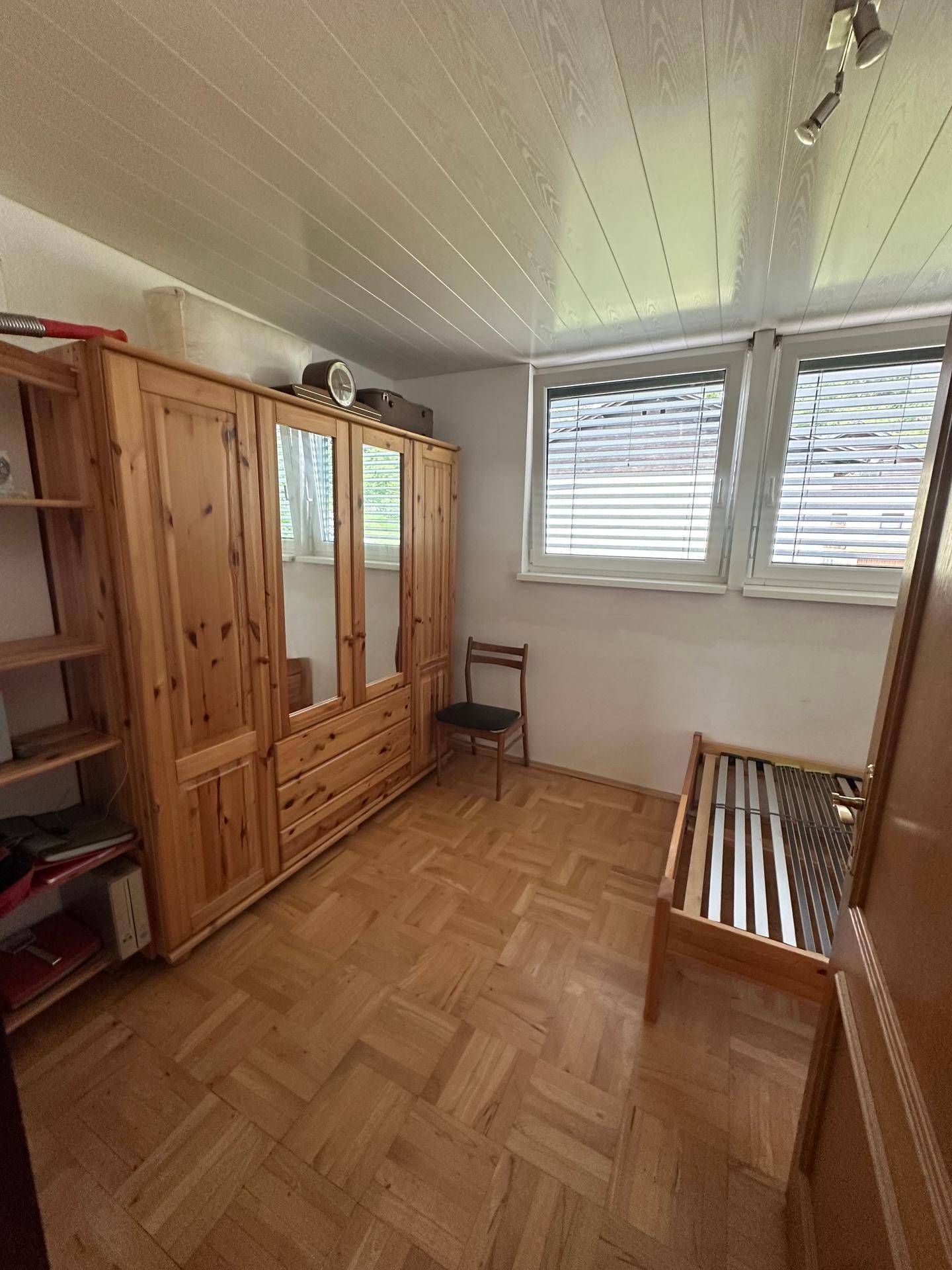 Schlafzimmer mit Holzschrank, Einzelbett und Parkettboden, bietet viel Stauraum.