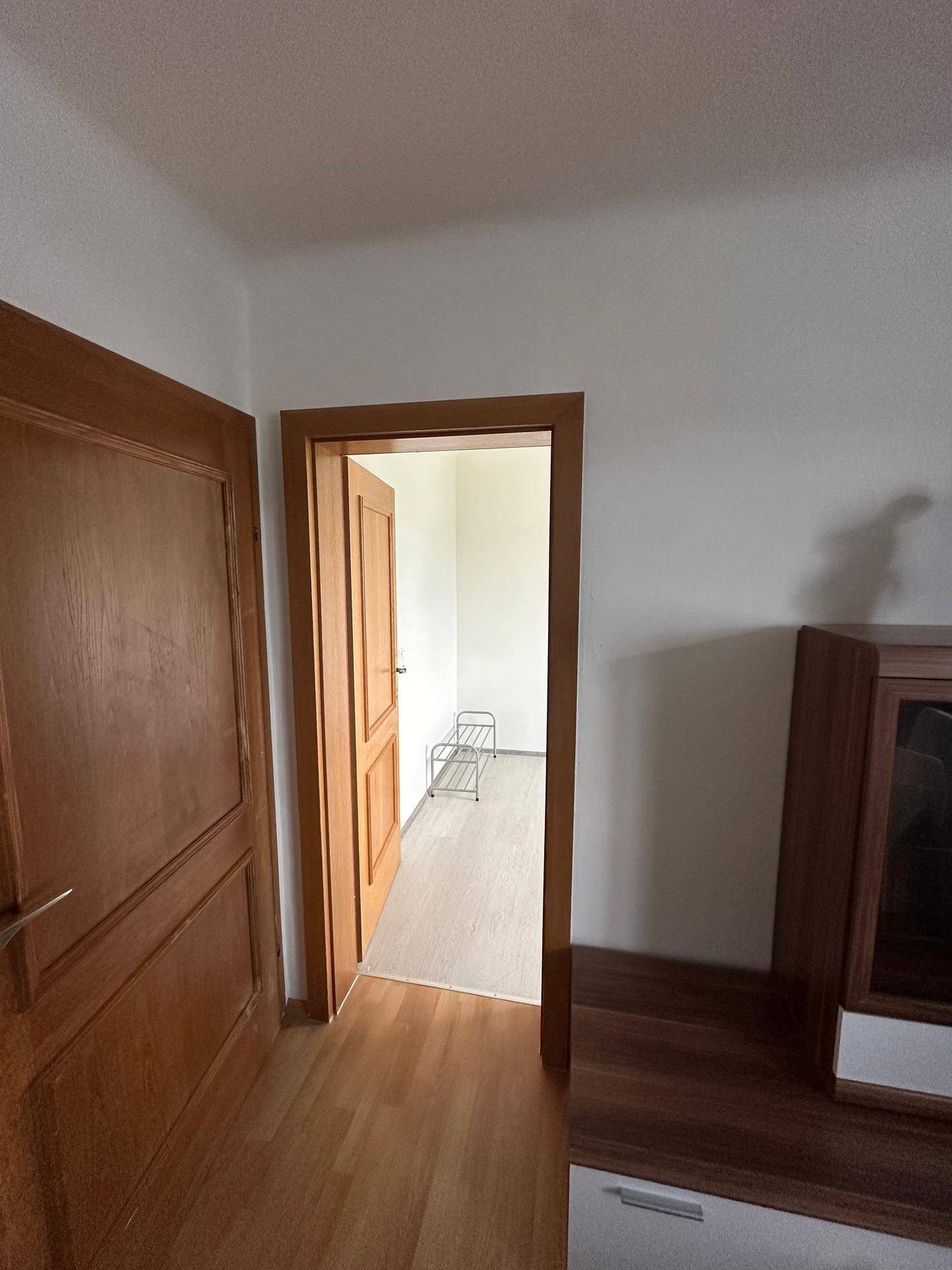 Blick durch eine Holztür in einen leeren Raum mit hellem Laminatboden.