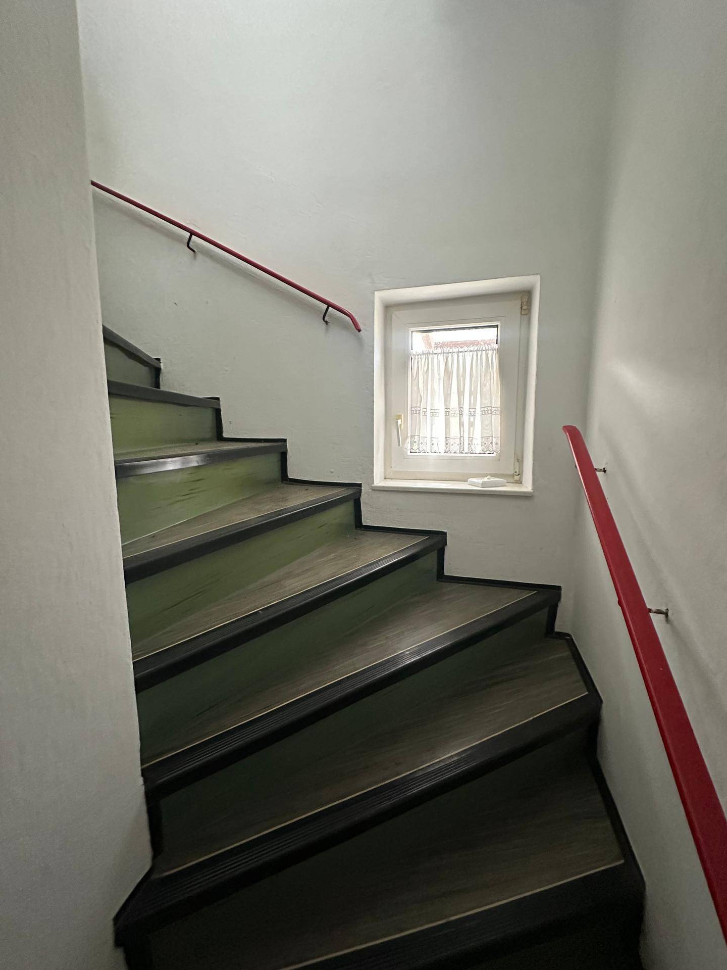 Treppenhaus mit Holzstufen und roten Handläufen, das zu den oberen Etagen führt.