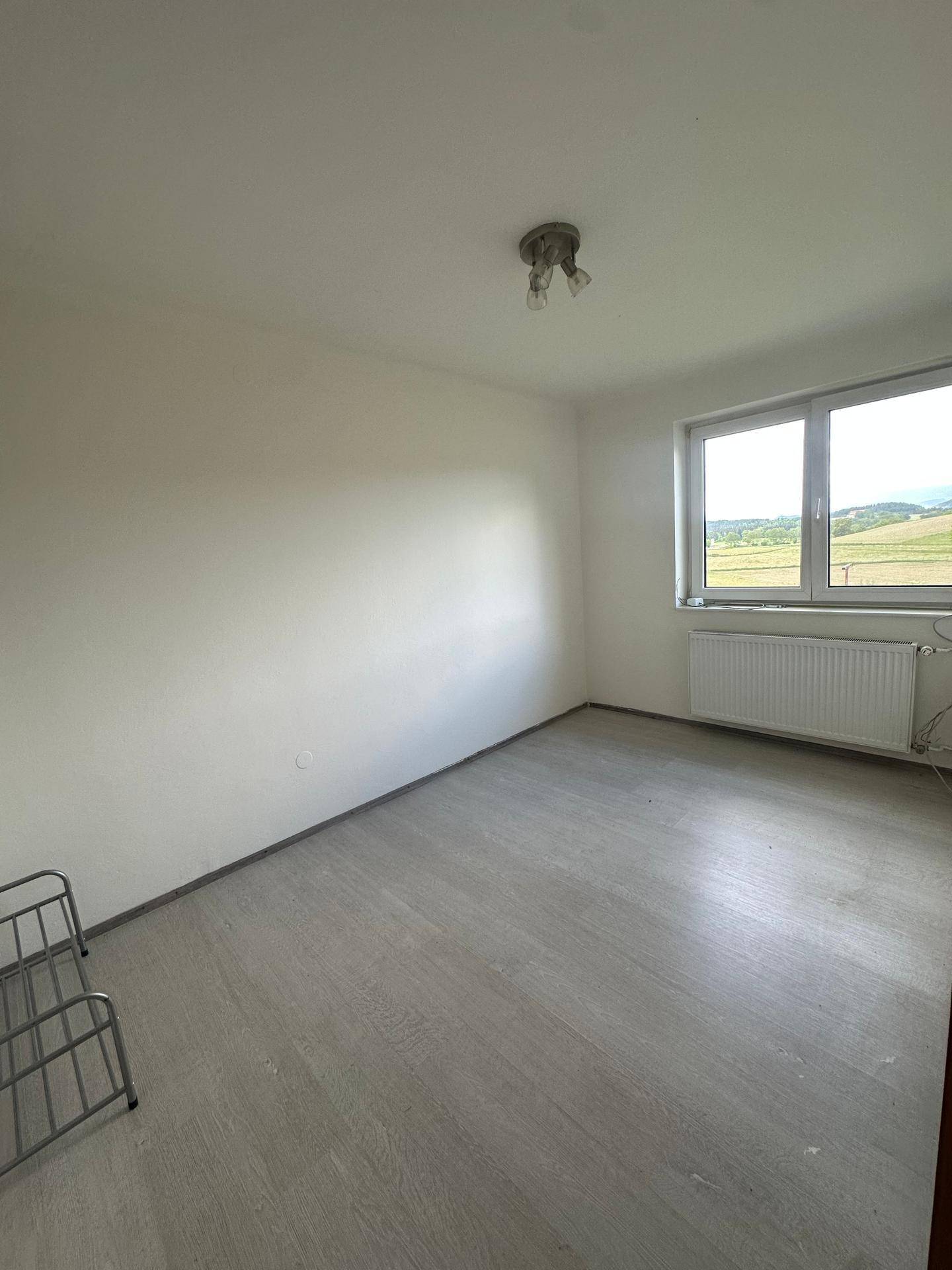 Helles Schlafzimmer mit Laminatboden und einem Fenster, das viel Tageslicht hereinlässt.